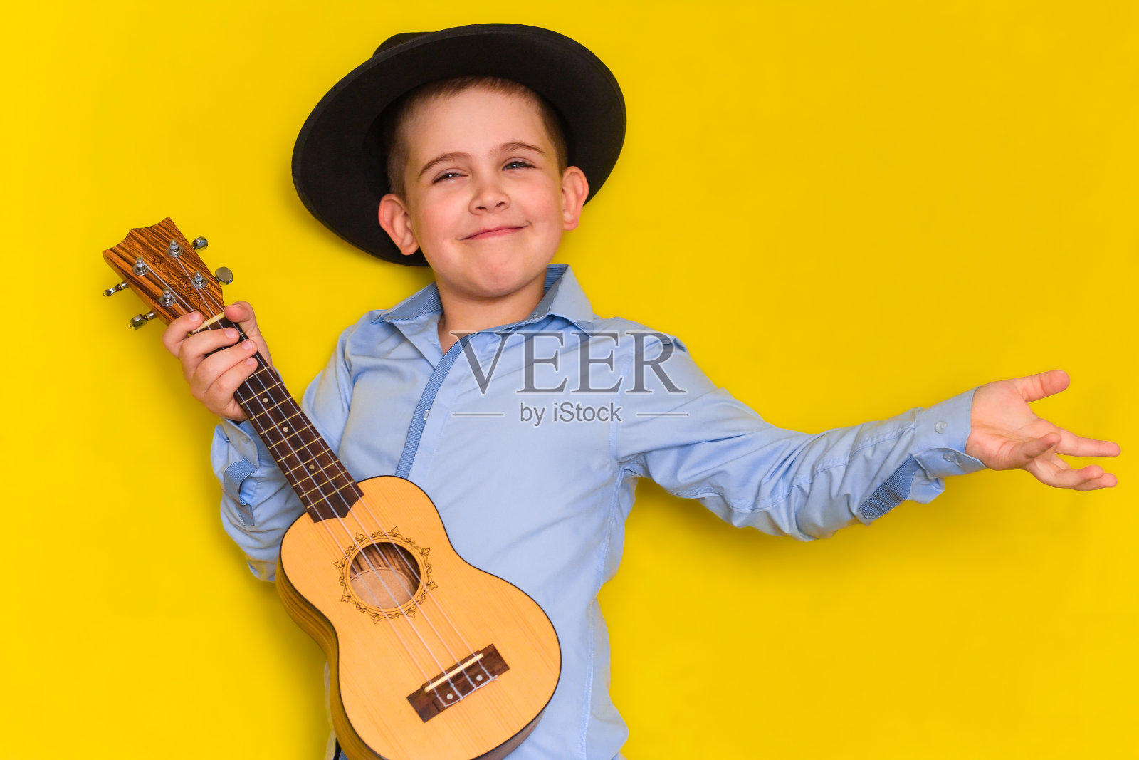 可爱的小男孩在帽子和衬衫保持吉他孤立在黄色背景照片摄影图片