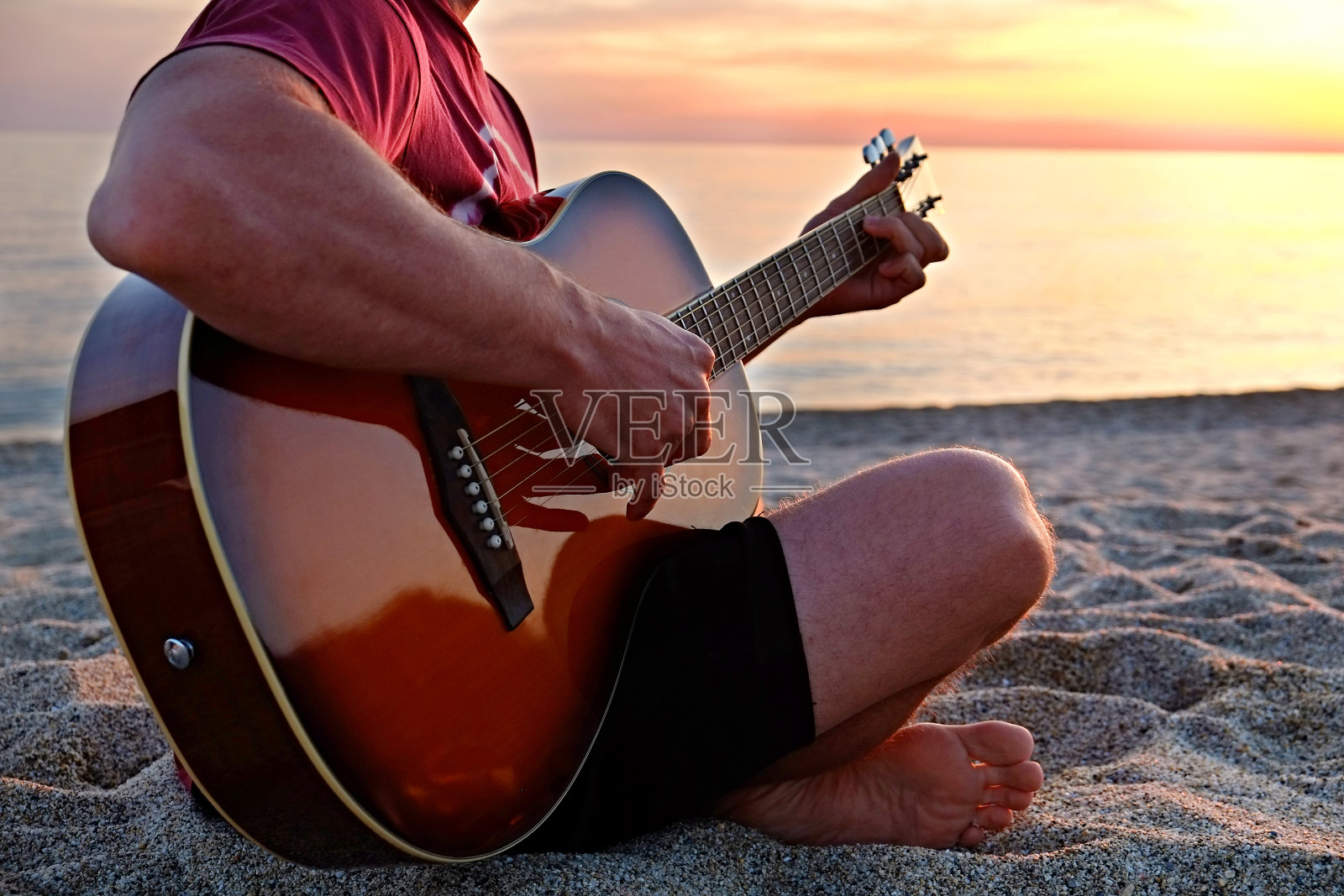 年轻人穿着紫色的扎染t恤，在美丽的日落时分，在海滩上弹无畏客厅的原声吉他。适合吉他手与日落的乐器在海边。背景，拷贝空间，关闭照片摄影图片