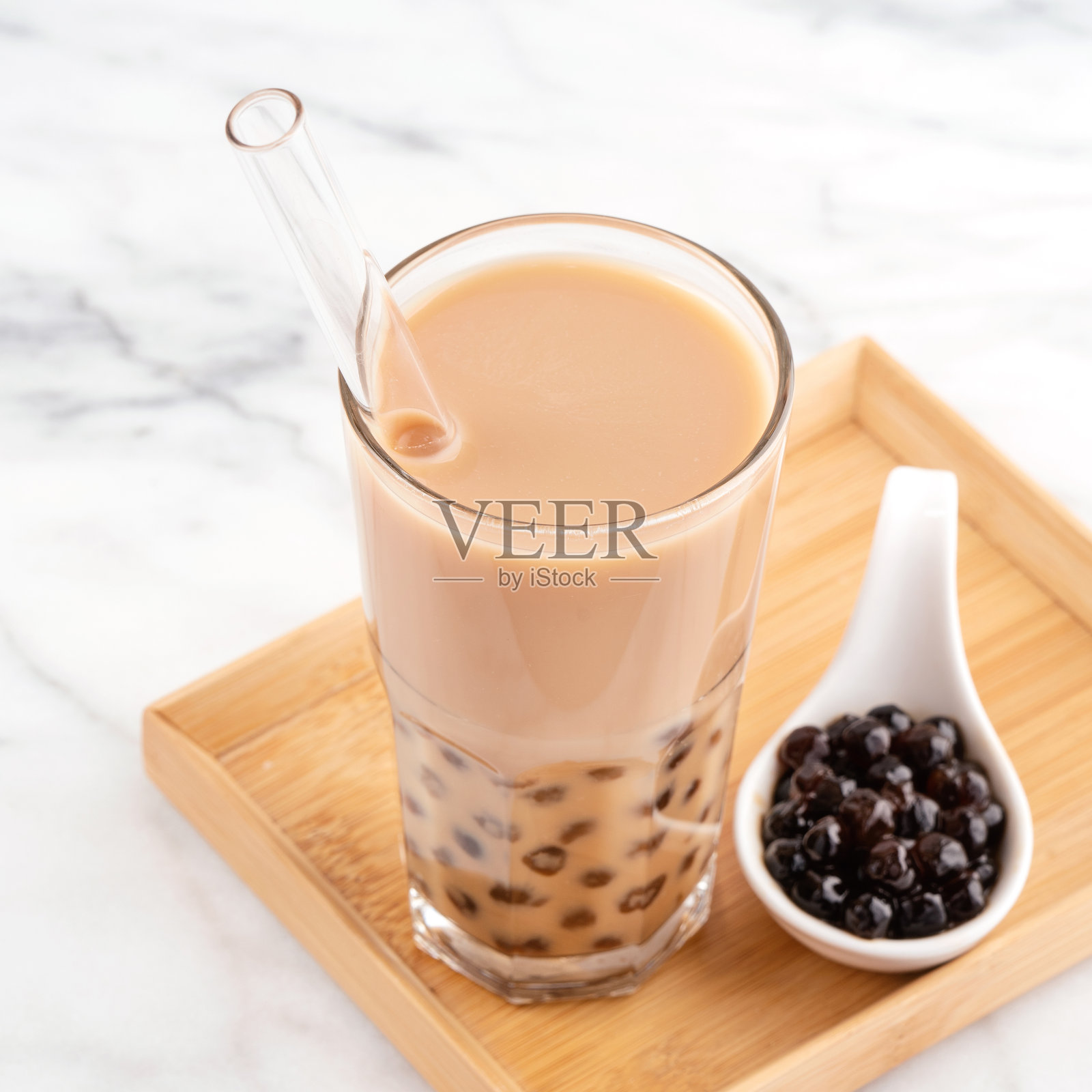 珍珠球奶茶在饮用玻璃与稻草在大理石白色桌子和木制托盘。照片摄影图片