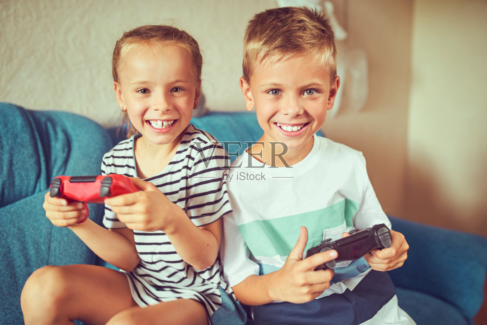 孩子们坐在沙发上情绪激动地玩电子游戏。照片摄影图片