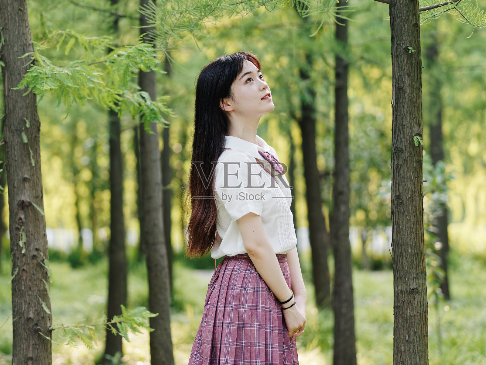 美丽的中国女孩的肖像在白色的衬衫和粉红色的裙子微笑和看在阳光灿烂的夏天森林，呼吸新鲜的空气和享受自然。美丽，生活方式和夏季概念。照片摄影图片
