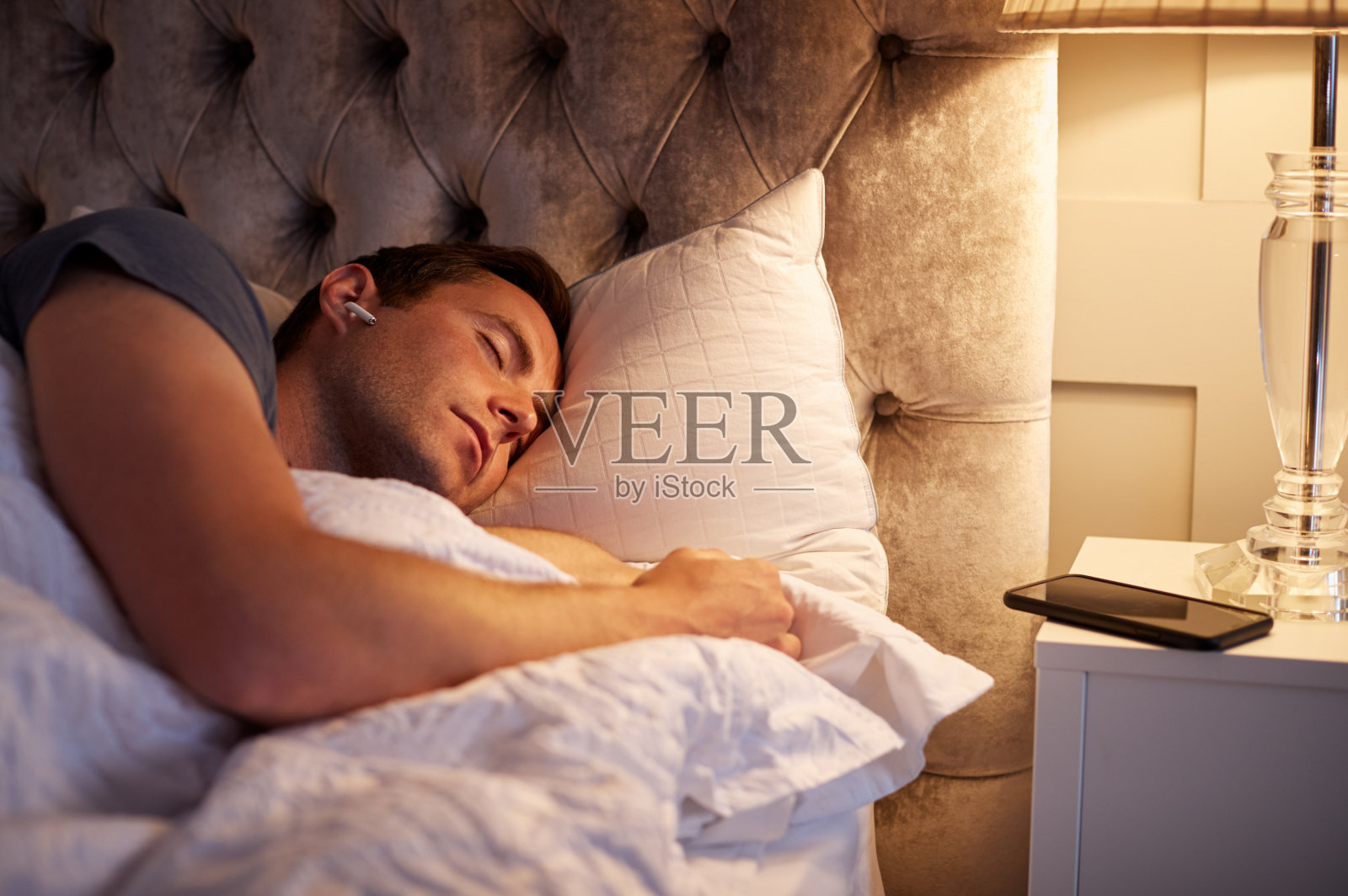 睡在床上的男人戴着与床边手机相连的无线耳机照片摄影图片
