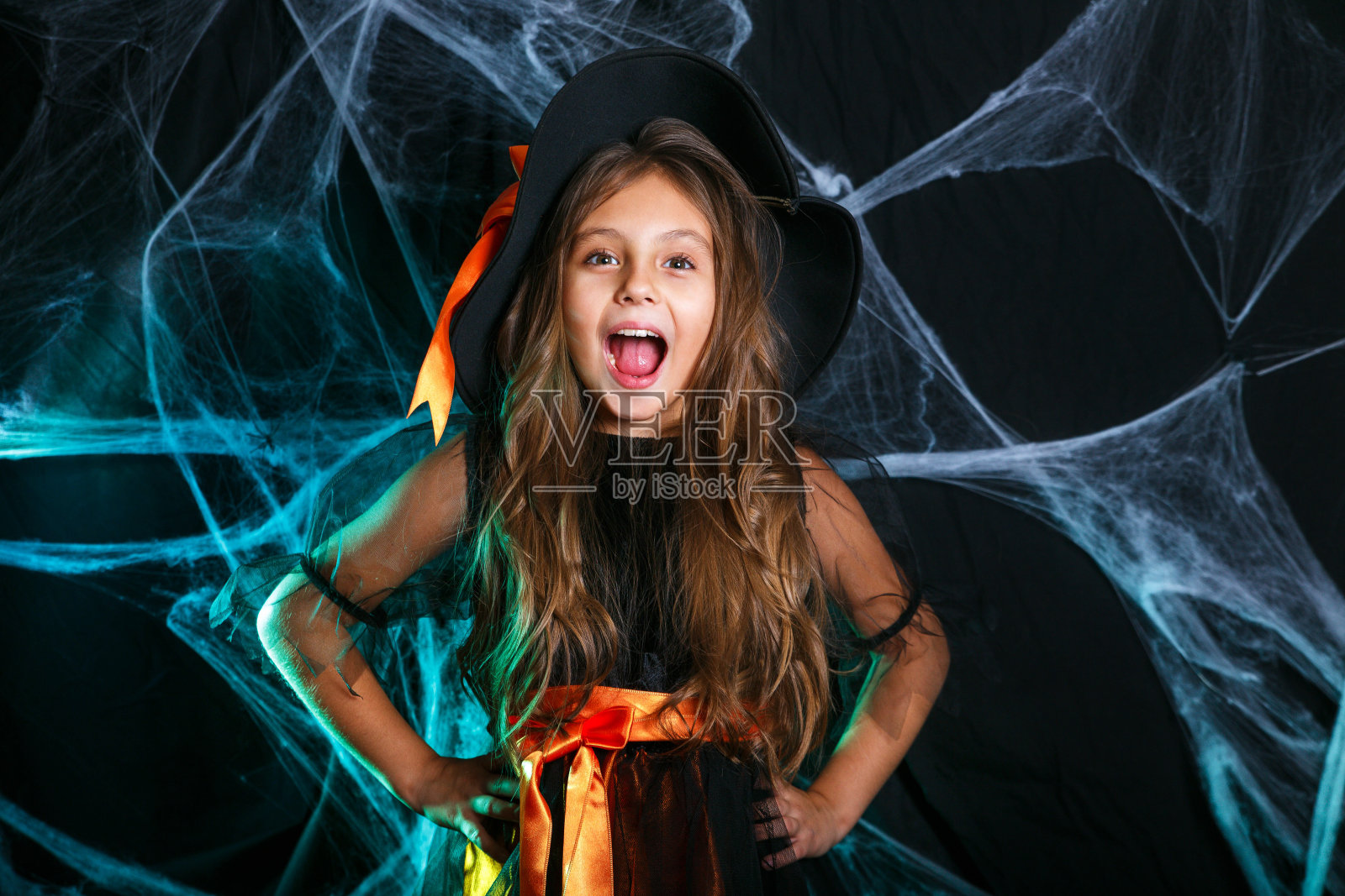 万圣节女巫概念-小女巫孩子在蜘蛛网和弯曲的南瓜背景上玩得很开心。照片摄影图片