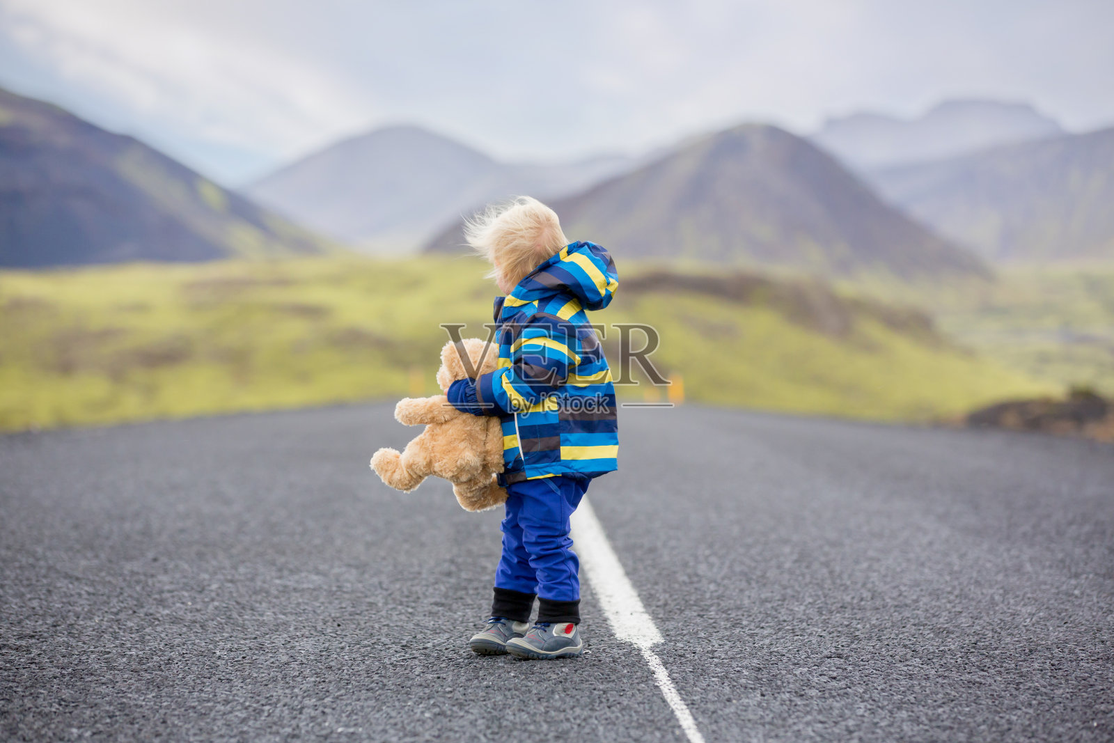 可爱的蹒跚学步的小男孩手拿泰迪熊，在冰岛的公路上奔跑照片摄影图片