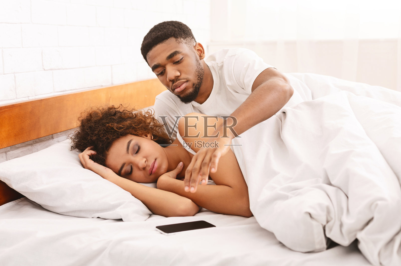 一个可疑的非洲男人在床上查看他妻子的手机照片摄影图片