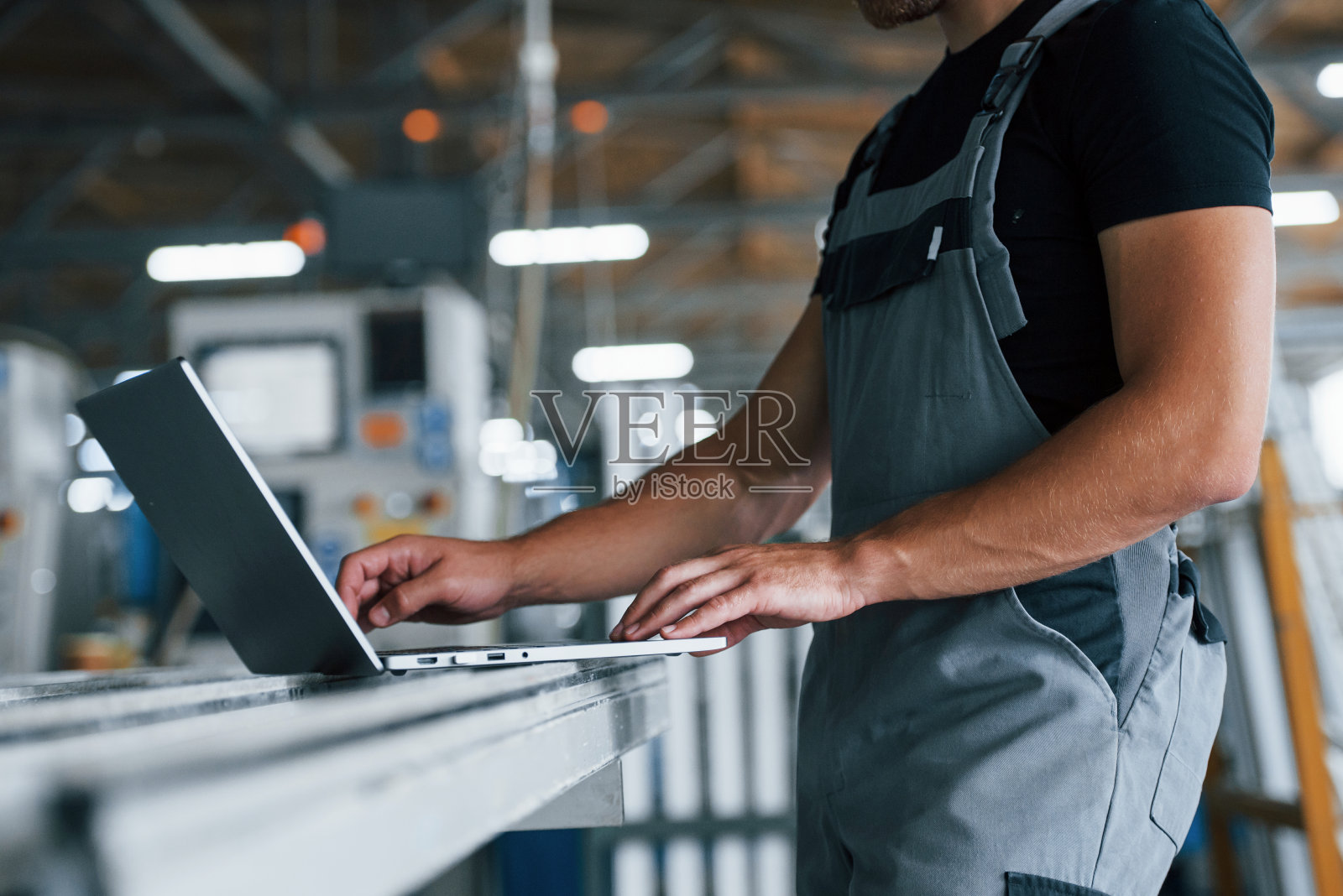 现代笔记本电脑。敲击键盘。工厂内的工业工人。戴着橙色安全帽的年轻技术员照片摄影图片