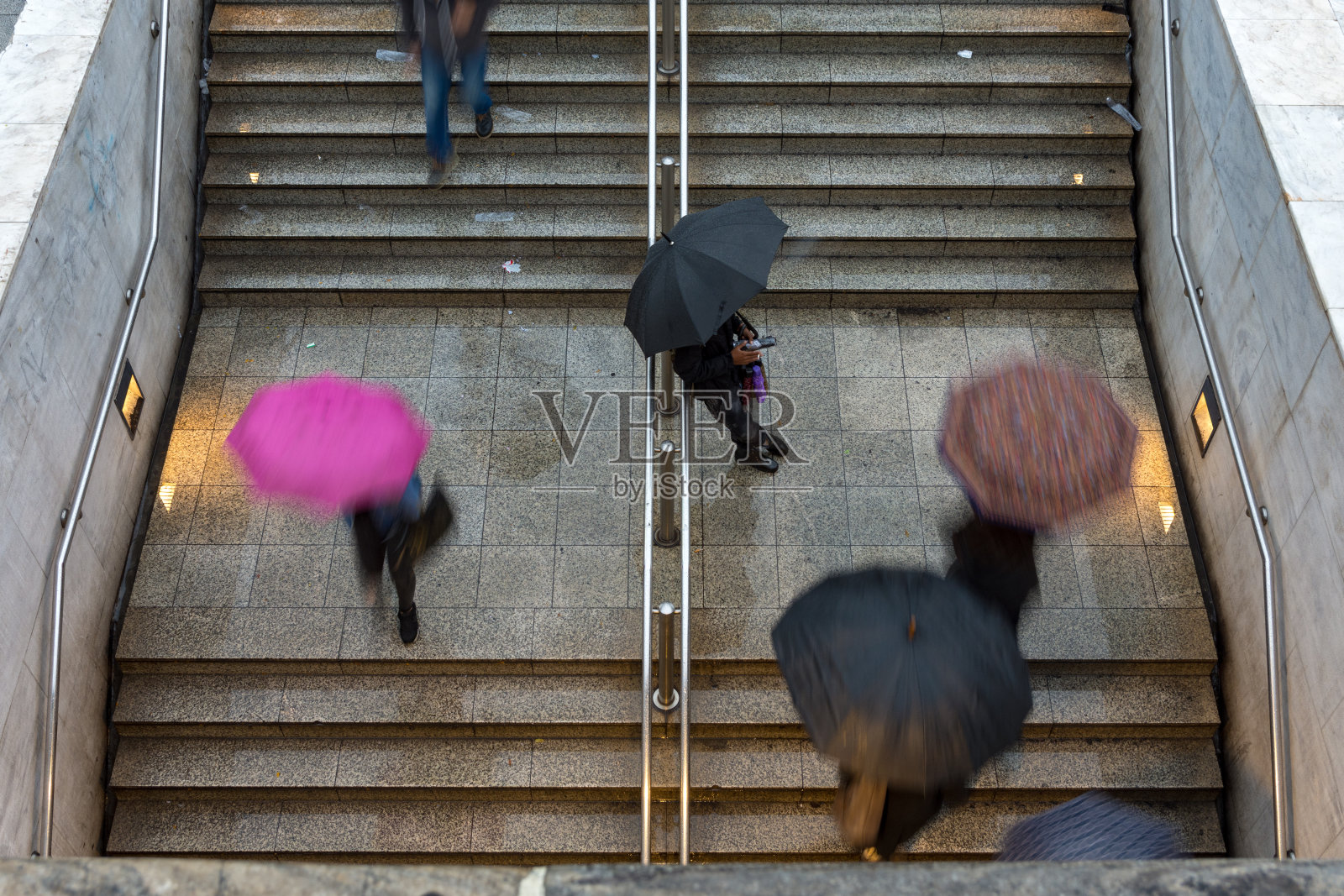 下雨时，人们在地铁站楼梯上撑着雨伞照片摄影图片