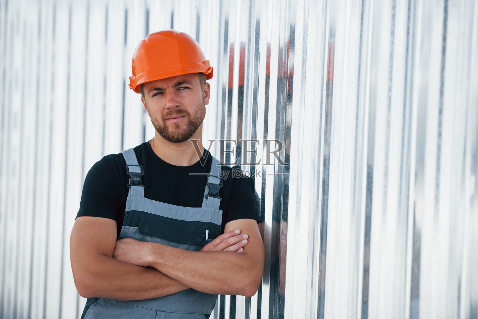 靠在墙上。严肃的产业工人在工厂的室内。戴着橙色安全帽的年轻技术员照片摄影图片