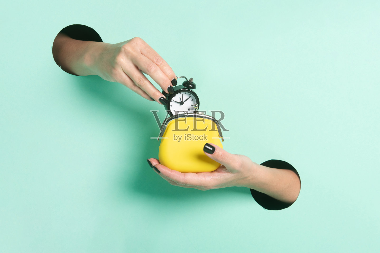 女人的手通过霓虹造币厂背景上的一个洞握住闹钟和钱包。极简主义创意孤立的时间是金钱的概念。照片摄影图片