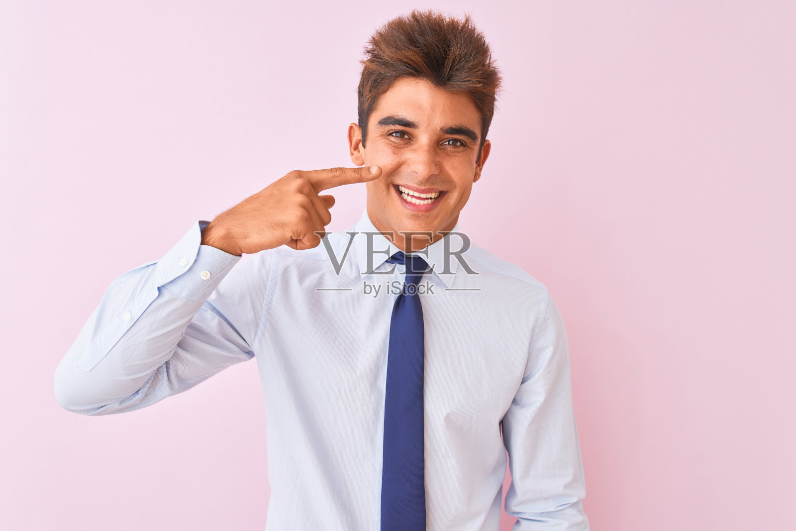 年轻英俊的商人穿着衬衫和领带站在孤立的粉红色背景，用手手指着脸和鼻子，笑得很开心。美丽的概念照片摄影图片