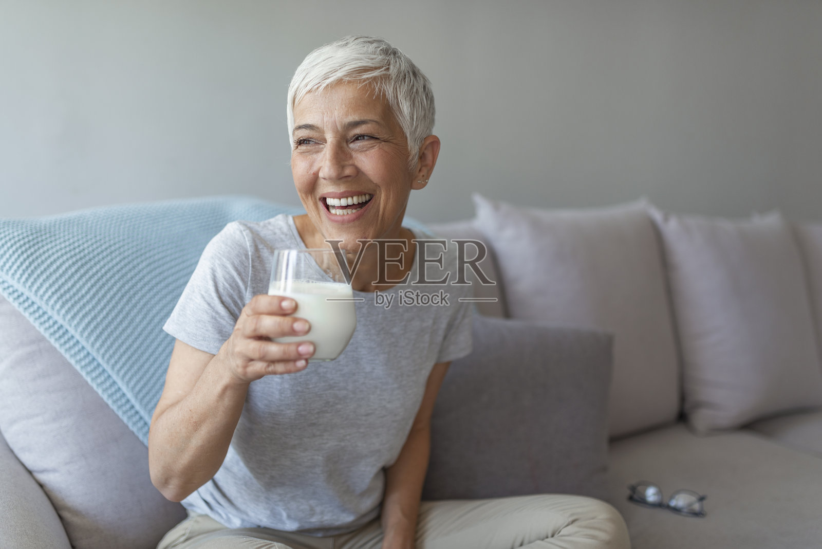 快乐的老女人在家里喝牛奶的时候玩。照片摄影图片