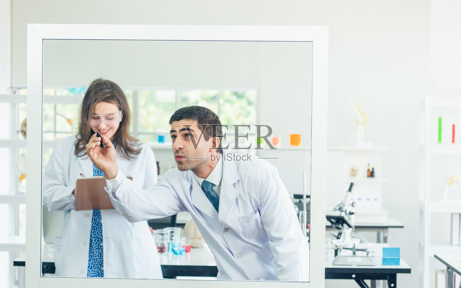 年轻的男女科学家在白板上写公式。他们在光明现代高科技实验室里解决科学问题。照片摄影图片