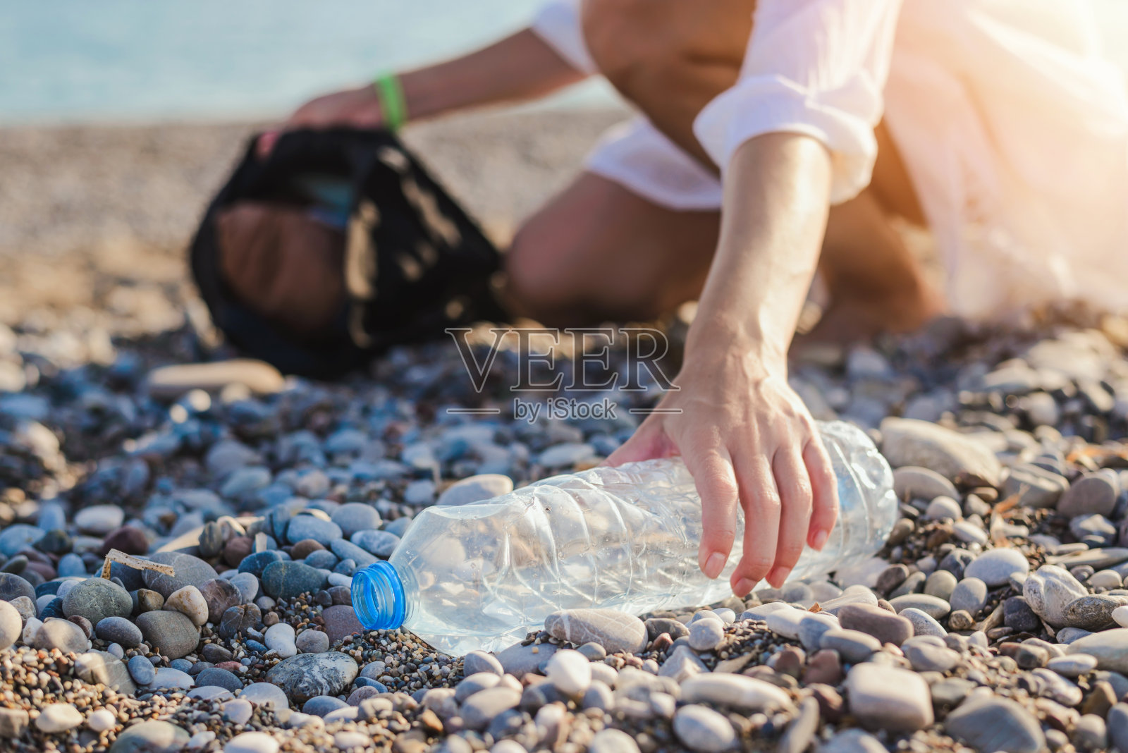 在海滩上收集塑料瓶的妇女。地球污染的概念。照片摄影图片