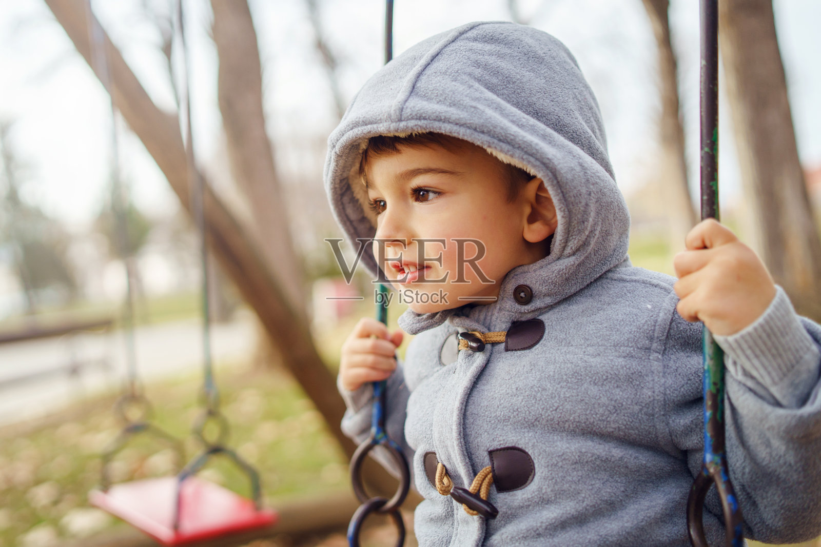 一个小可爱的三岁白人男孩的肖像在冬天或秋天穿着大衣在公园的秋千上玩照片摄影图片