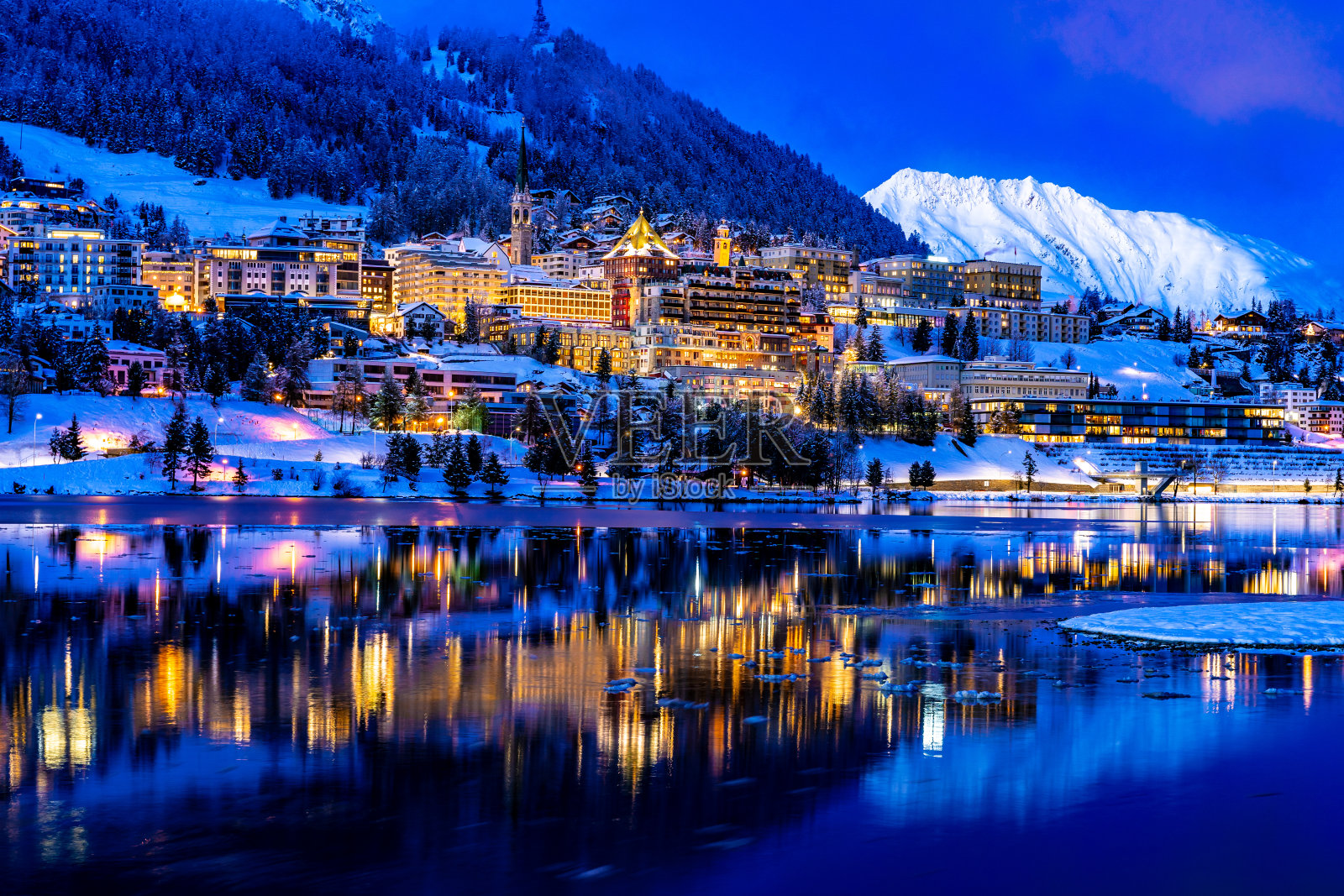 在瑞士圣莫里茨美丽的夜晚灯光，从湖和雪山的反射在背景照片摄影图片