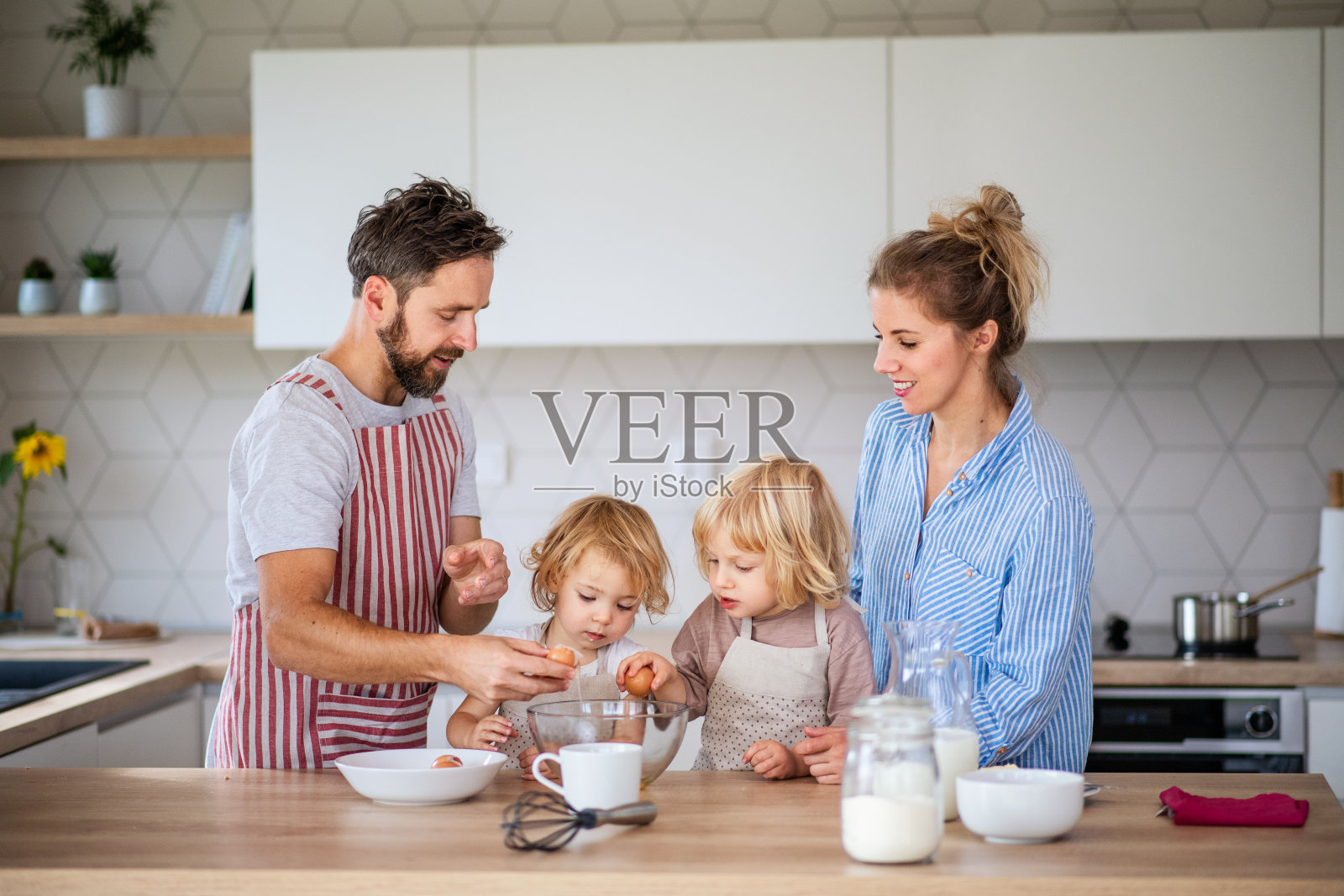 年轻的家庭和两个小孩在厨房里做饭。照片摄影图片