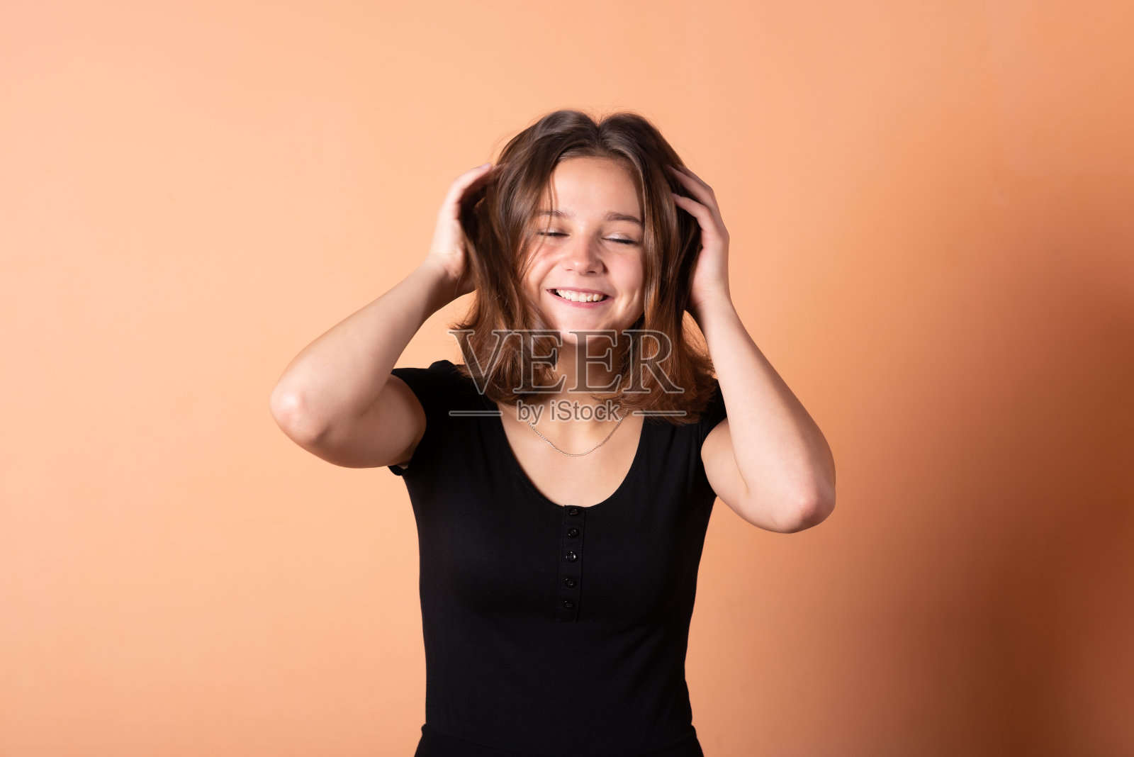 女孩在浅橙色的背景下把头发拉直。照片摄影图片