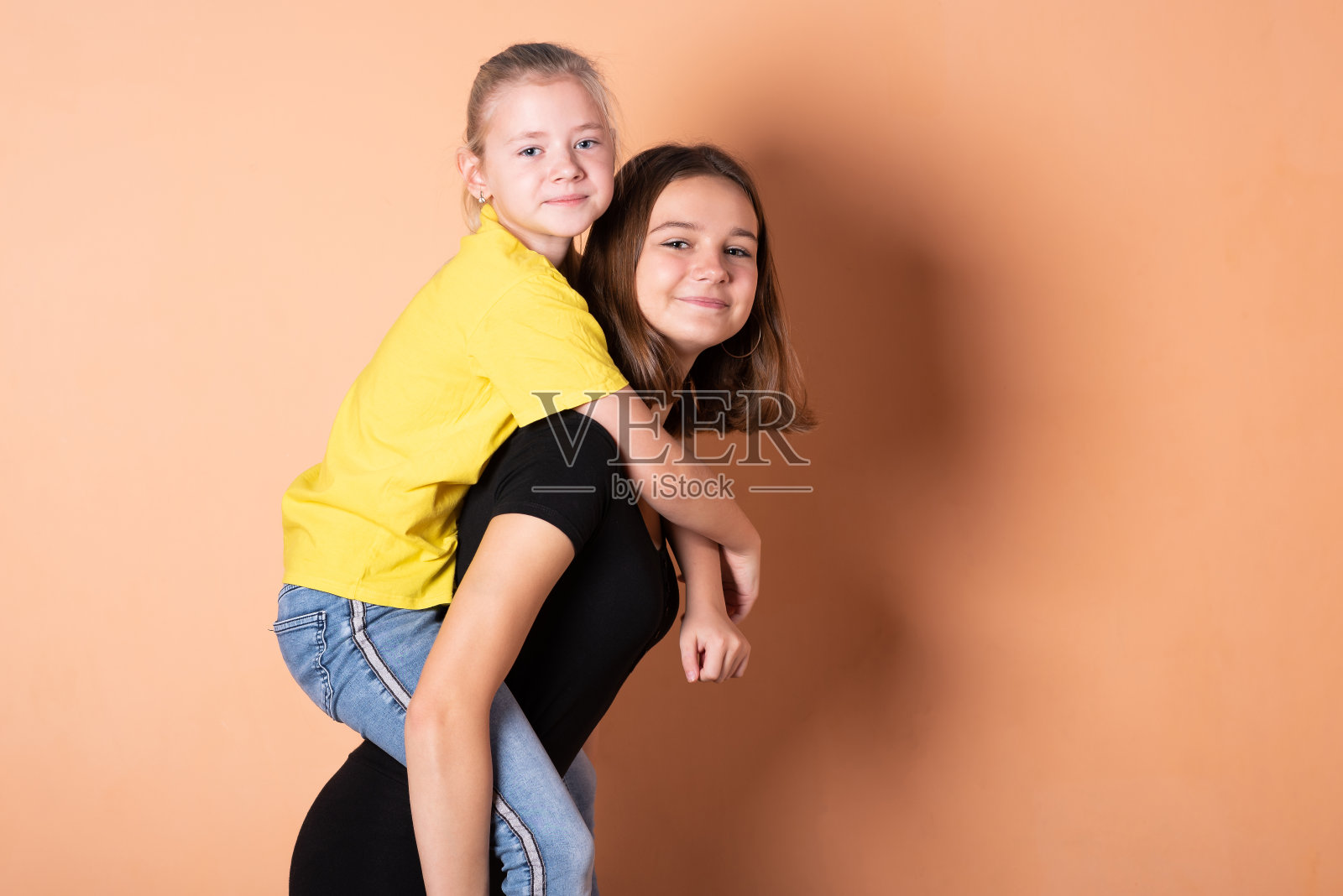 两个女孩，姐妹，一个在另一个的肩膀上，在浅橙色的背景上。照片摄影图片