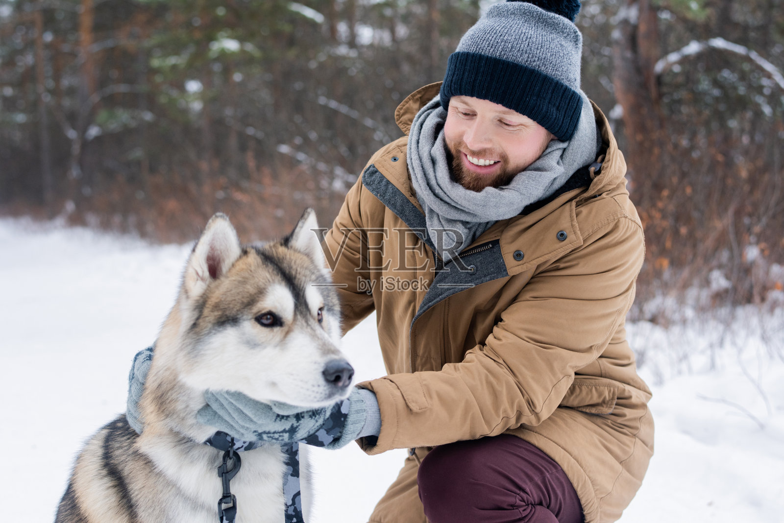 年轻的微笑男子在冬装拥抱纯种西伯利亚哈士奇狗照片摄影图片
