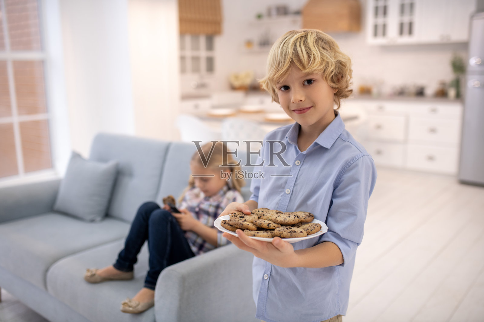 男孩拿着一盘饼干站着，女孩坐在沙发上照片摄影图片