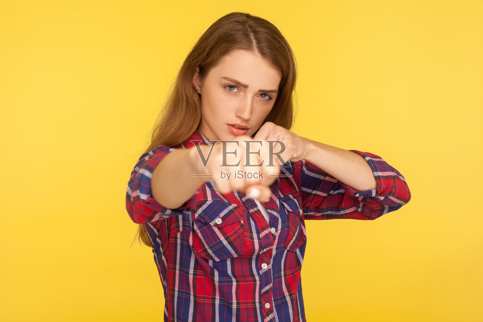 肖像强壮和决心的姜黄色女孩在格子衬衫打击空气拳头和看自信的镜头照片摄影图片