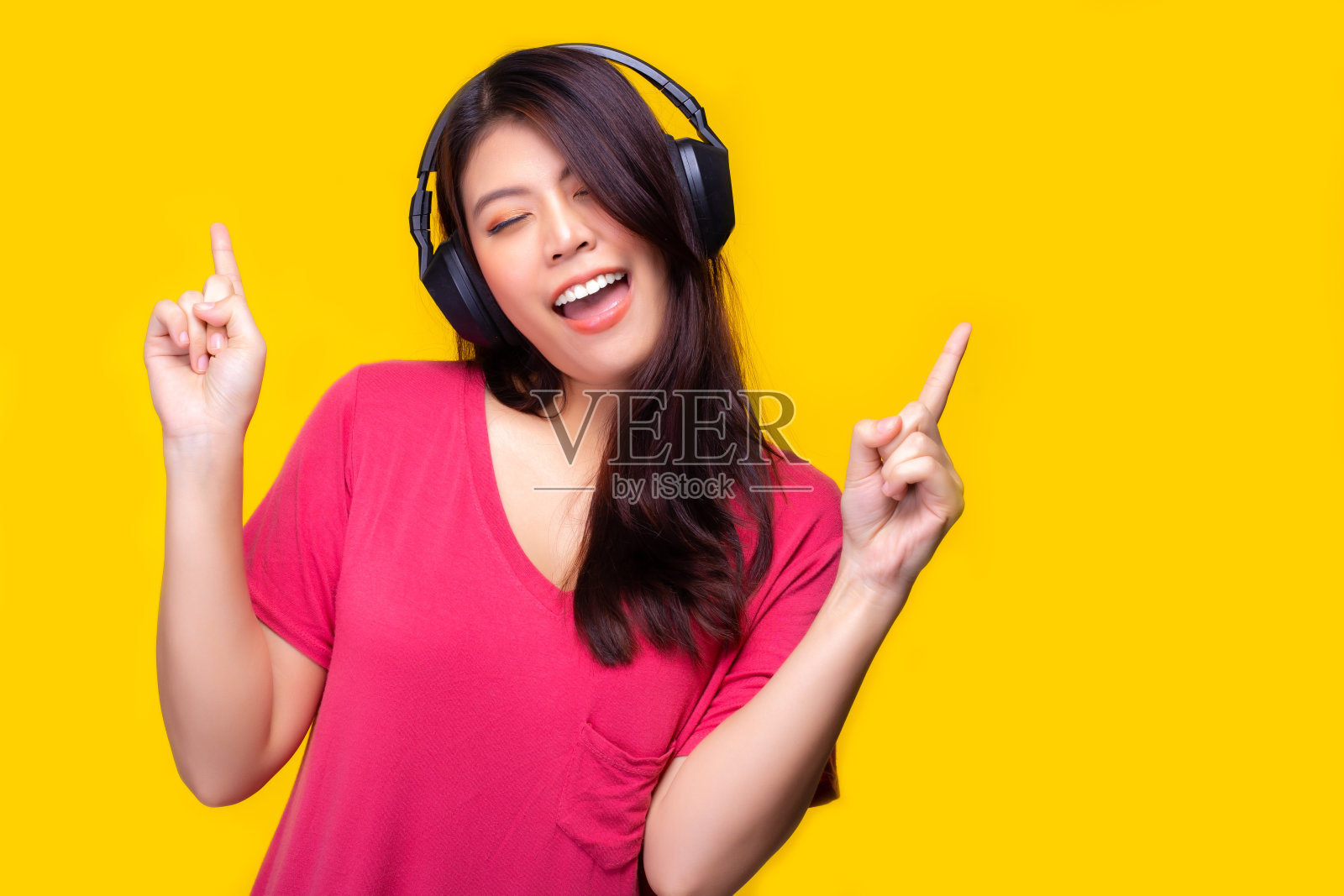 亚洲女人听着音乐，用幸福唱着歌，微笑着面对。迷人美丽的年轻女孩喜欢唱歌和听音乐，让她快乐，放松的时间。黄色背景,丰富多彩照片摄影图片