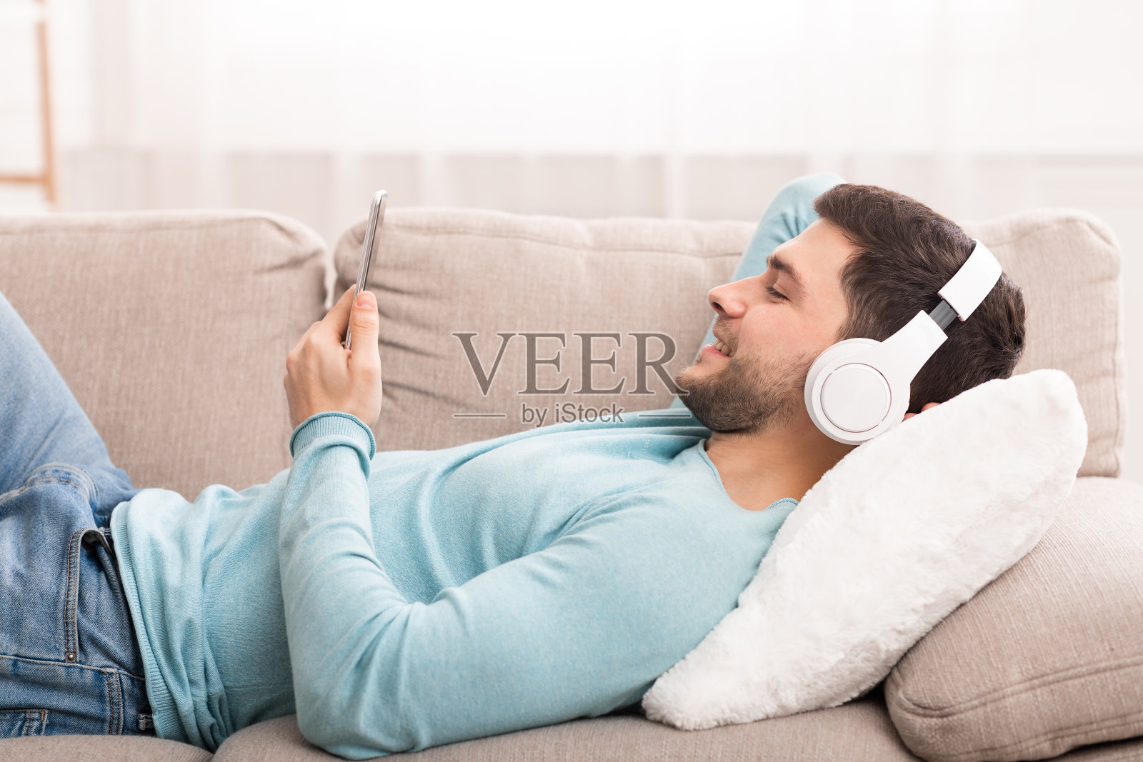 躺在家里沙发上戴耳机玩智能手机的家伙照片摄影图片