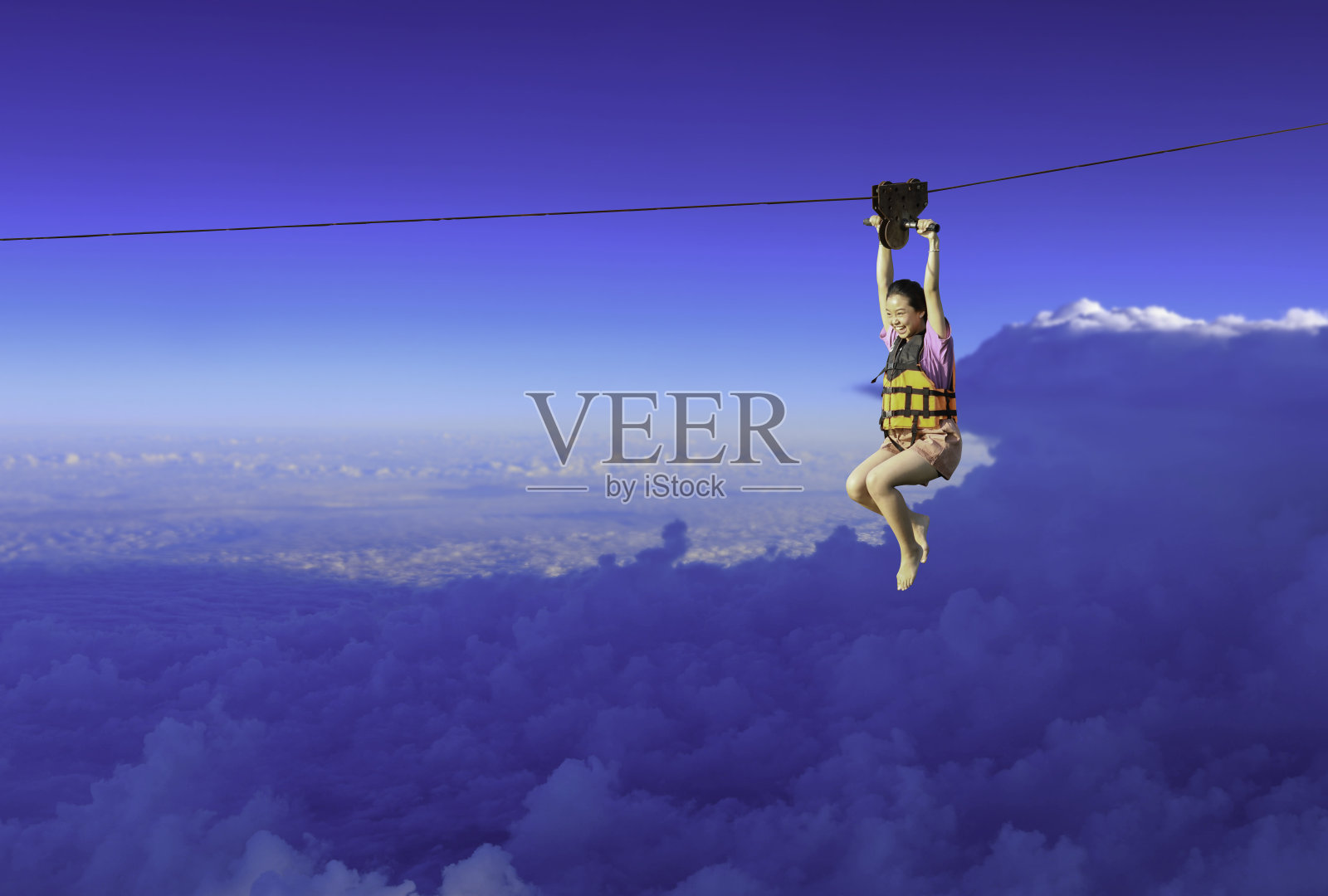 令人兴奋的冒险活动。在蓝天背景下，一个小女孩吊在滑索上。照片摄影图片