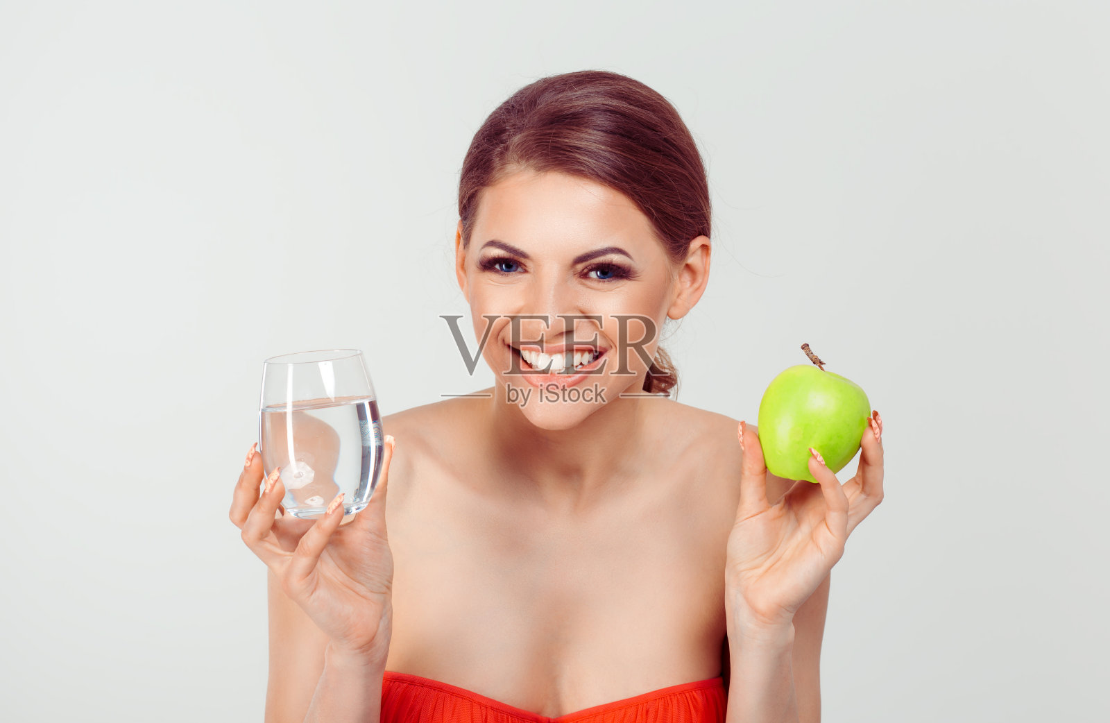 快乐的女人手里拿着一个苹果和一杯水，背景是白色的照片摄影图片