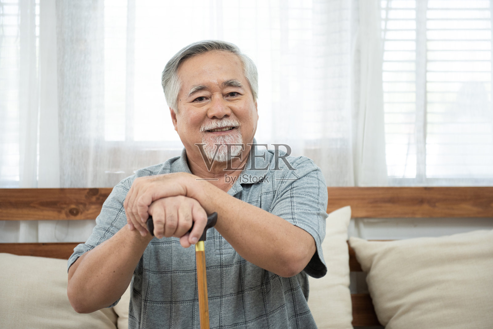 年长的亚洲男人坐在教练的肖像，手握帮助手杖，坐在沙发上，看着相机与幸福和健康的生活方式。照片摄影图片