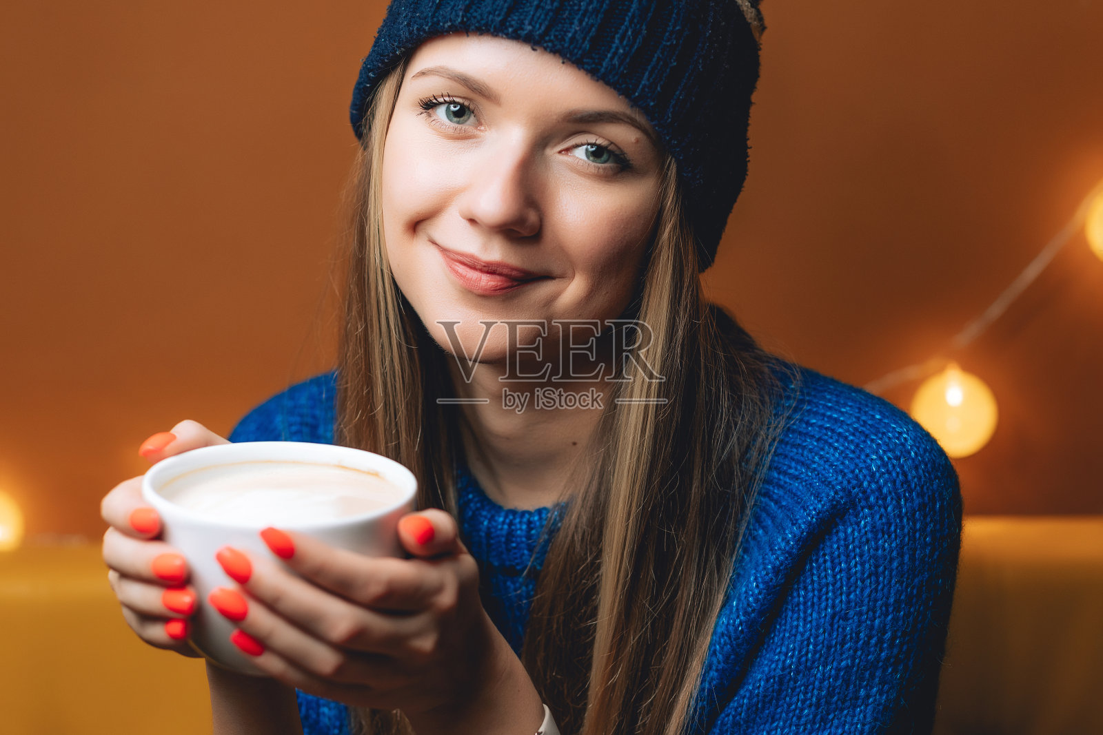 在咖啡馆或办公室里的美丽快乐的女人。她穿着蓝色的毛衣。为您的设计复制空间。概念杯饮料和礼品照片摄影图片