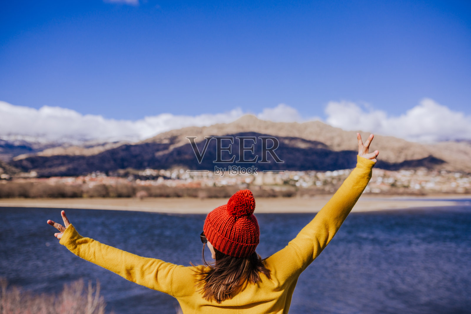 一个年轻的白人女人在阳光明媚的日子里站在山上。美丽的湖背景视图。自然的概念。后视图照片摄影图片
