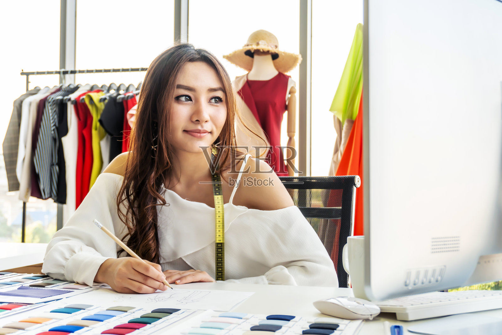 亚洲女设计师在工作室的设计师办公桌上思考并在纸上画一些东西，供客户定购物品。服装设计师在办公室工作。公司设计师的概念。照片摄影图片