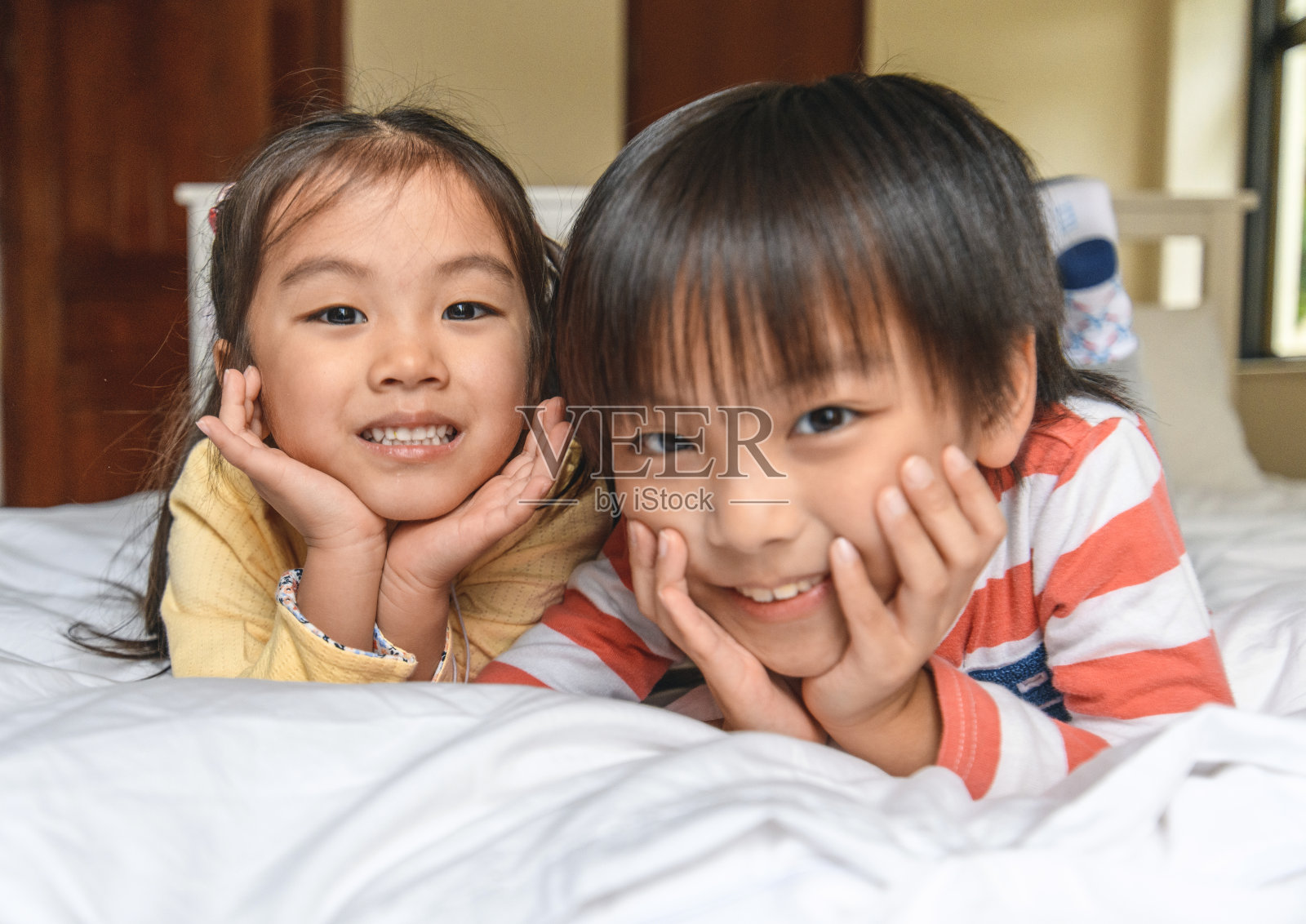 微笑的年轻的中国兄弟姐妹在凌乱的床上休息照片摄影图片