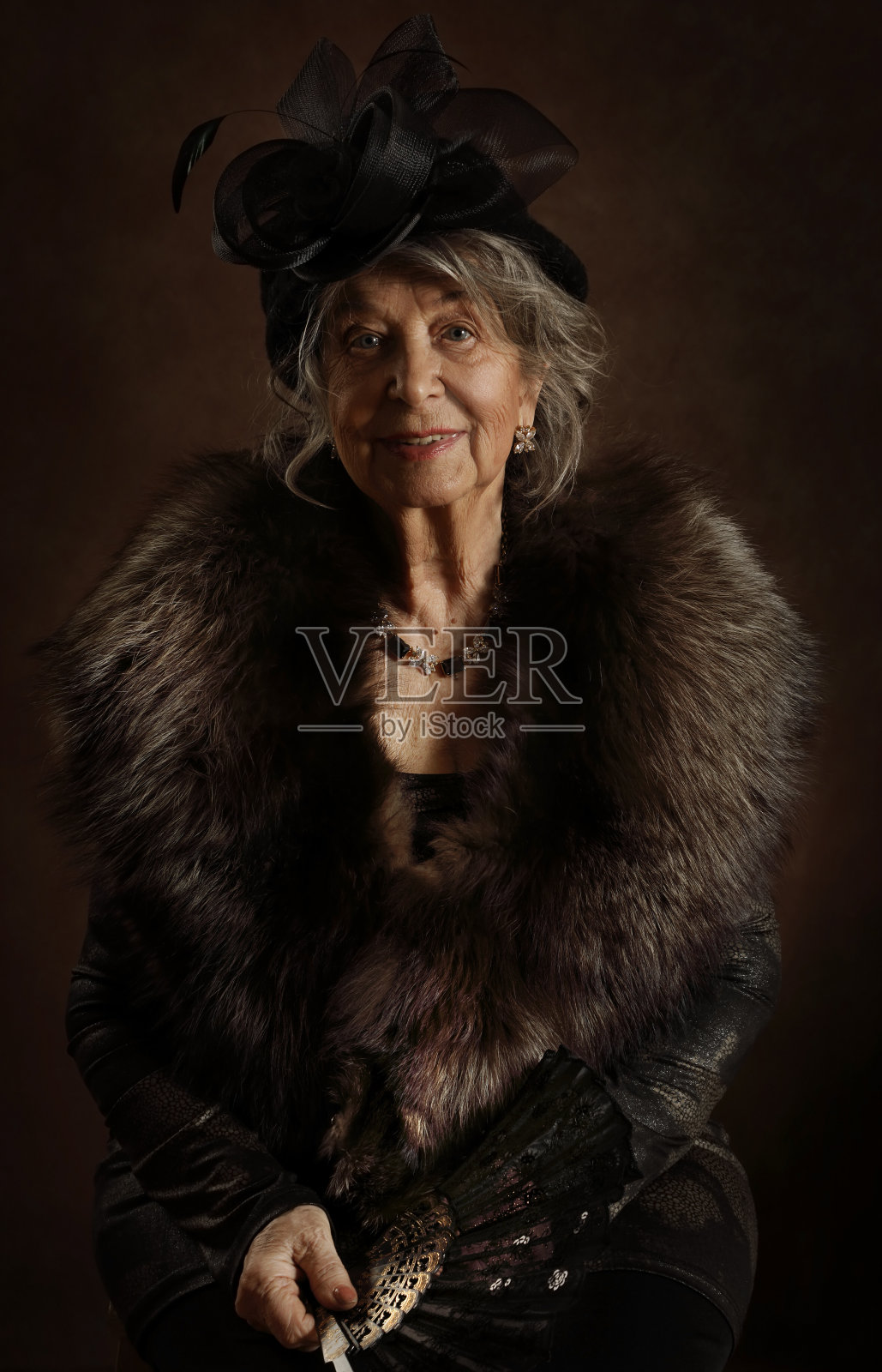 一个棕色背景上拿着扇子的老妇人的肖像照片摄影图片