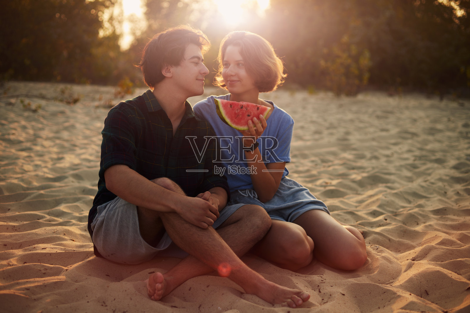 日落时分，年轻的白人女子和男子在海滩上吃西瓜。照片摄影图片