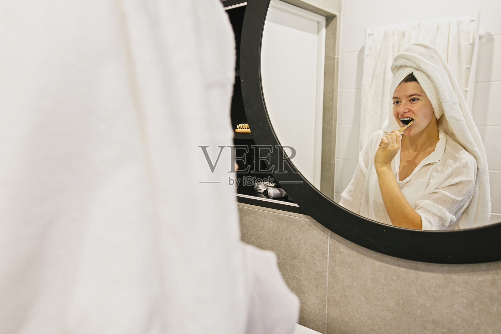 口腔卫生。“零浪费”。美丽的年轻女子在白毛巾刷她的牙齿竹牙刷和木炭牙膏在现代浴室，看着圆镜。照片摄影图片