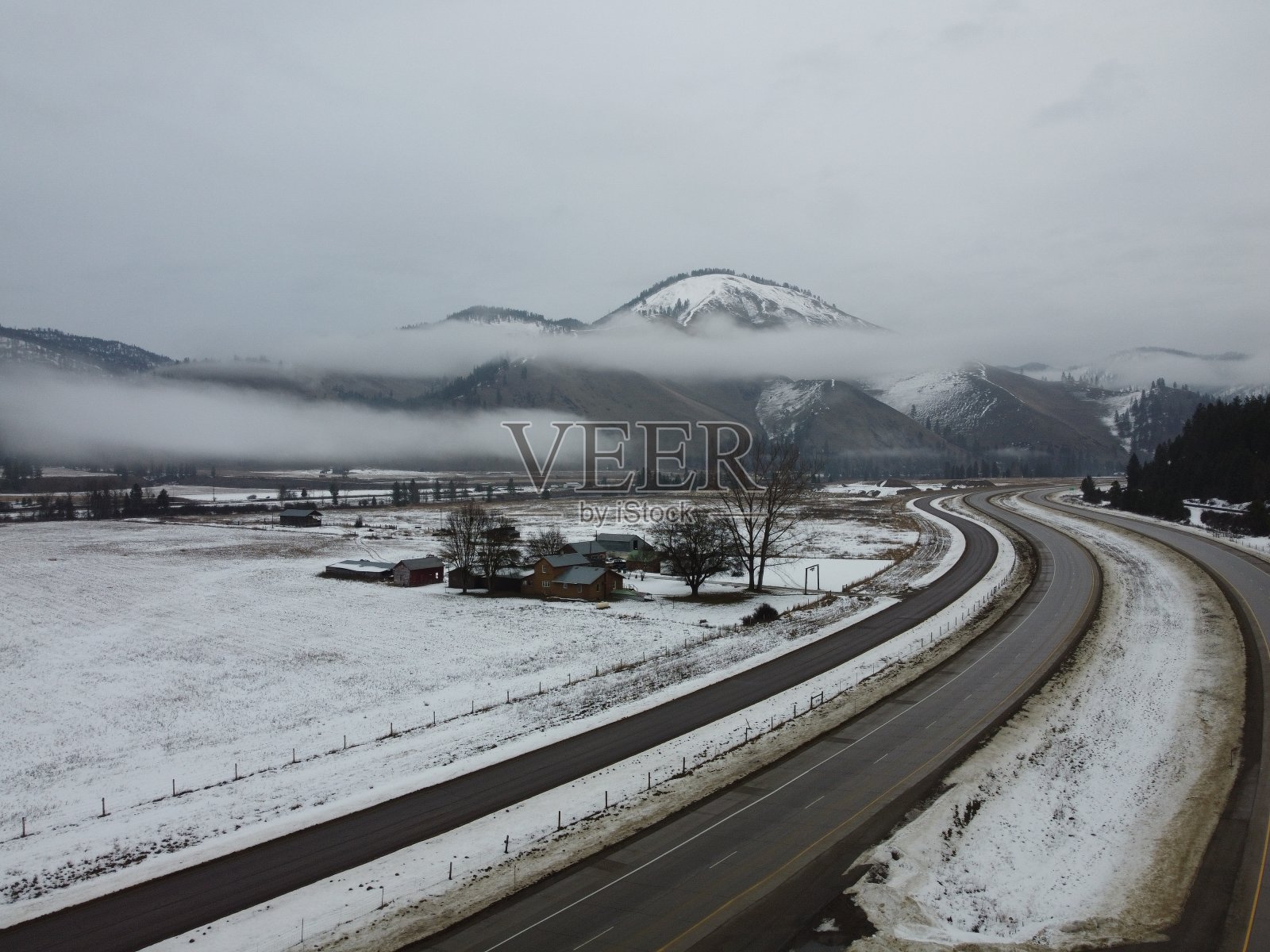 弯弯曲曲的道路通向迷雾笼罩的雪山，前景是牧场的家照片摄影图片