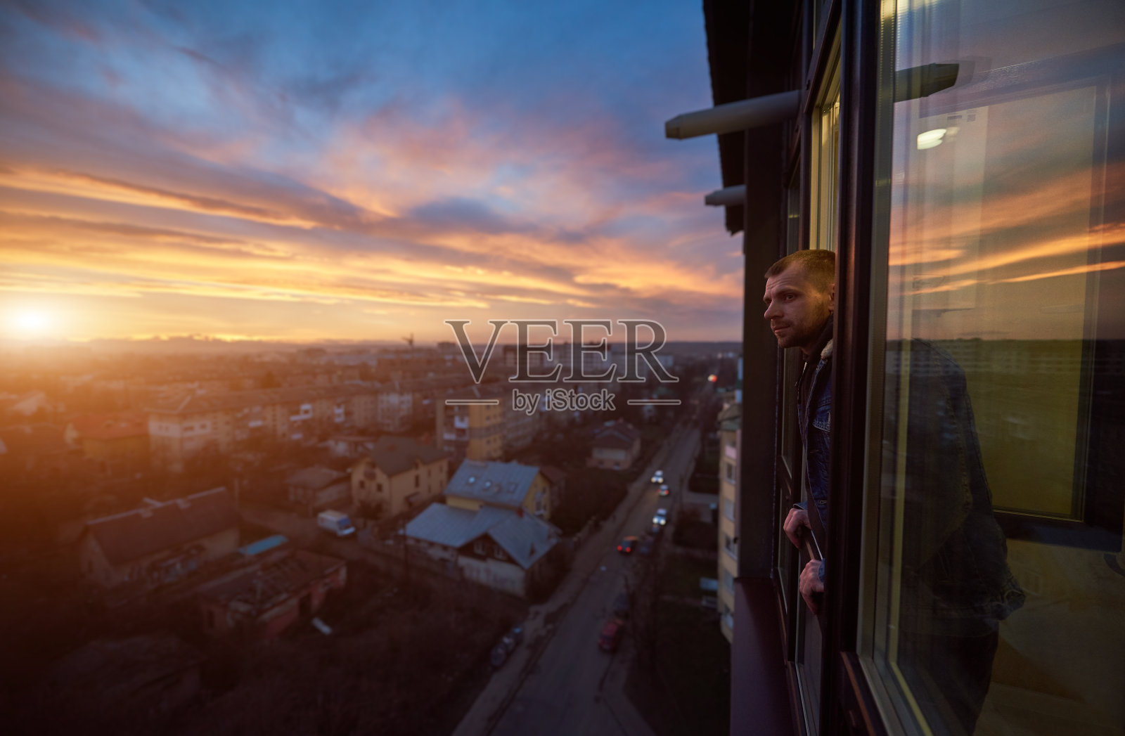 夕阳西下时，一个微笑的男人从阳台往外看。美丽的城市风景照片摄影图片