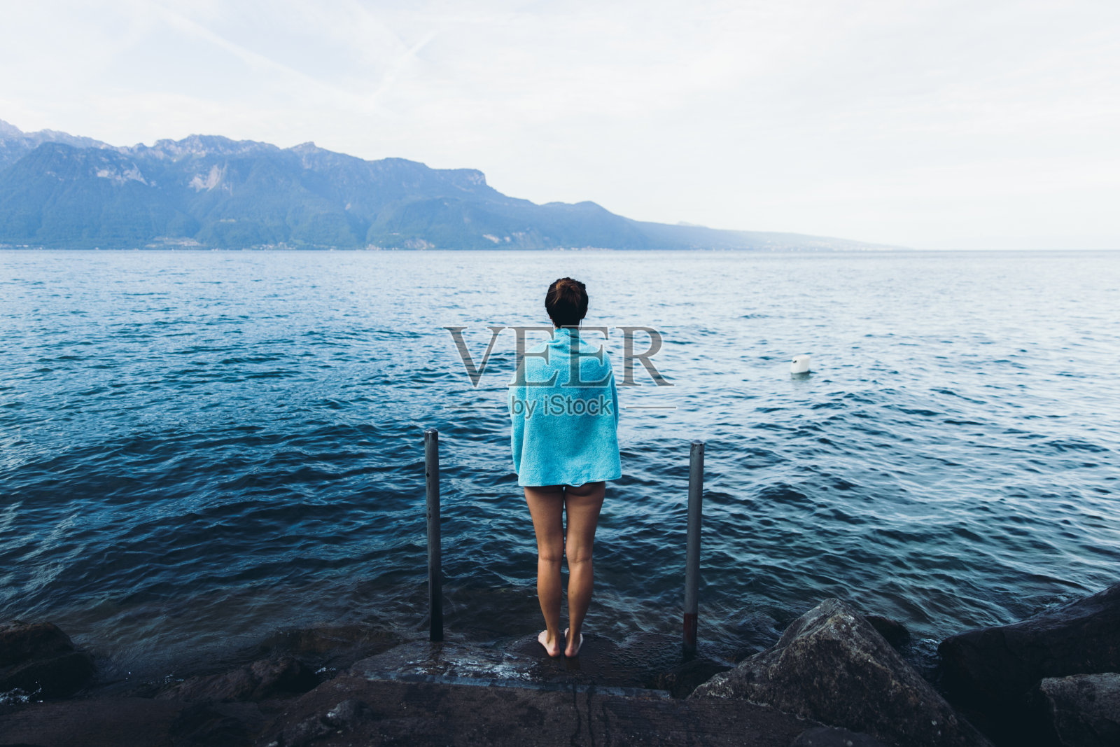 在瑞士的湖滨，一名女子在山湖游泳后裹着毛巾休息照片摄影图片