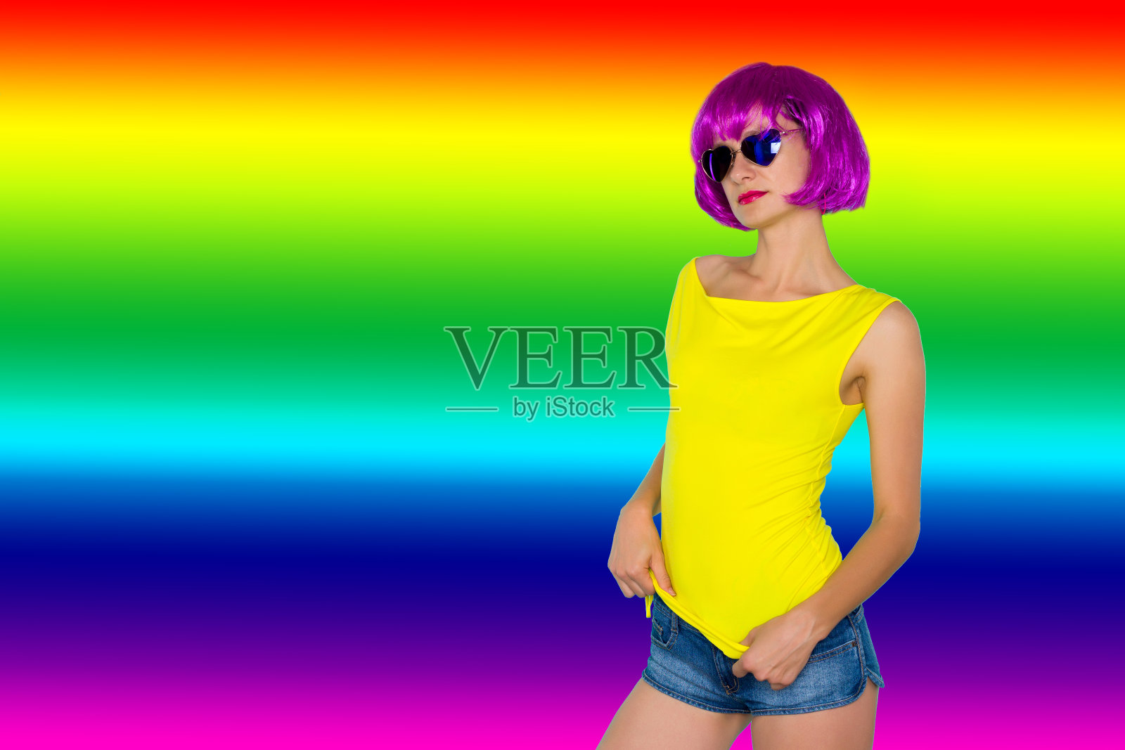 年轻女子的肖像在粉红色的假发和太阳镜，黄色的t恤在彩虹的背景照片摄影图片