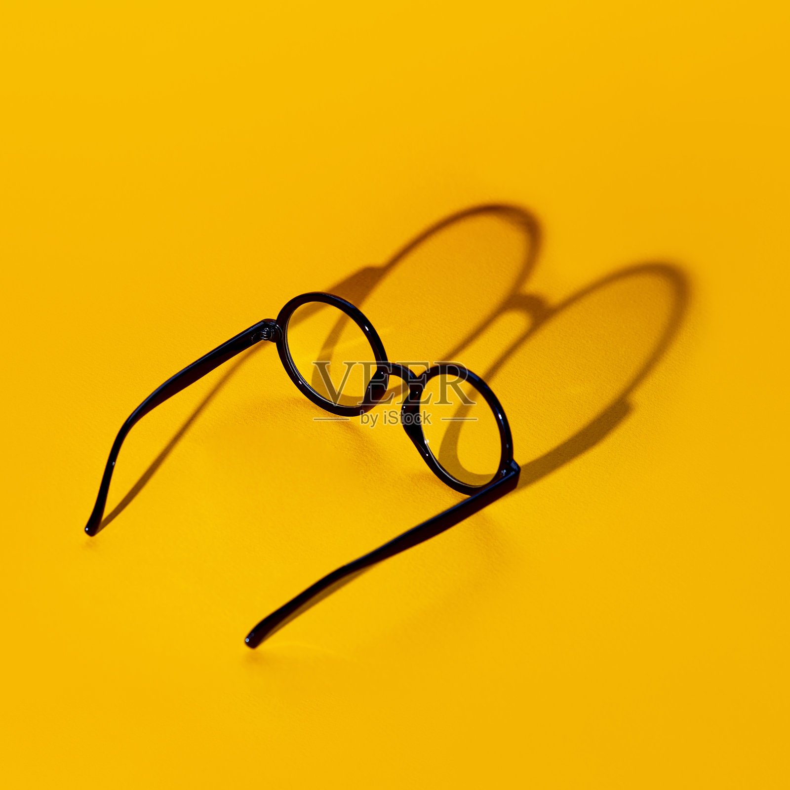 黑色的圆眼镜上的黄色背景与硬阴影和题字的外观照片摄影图片