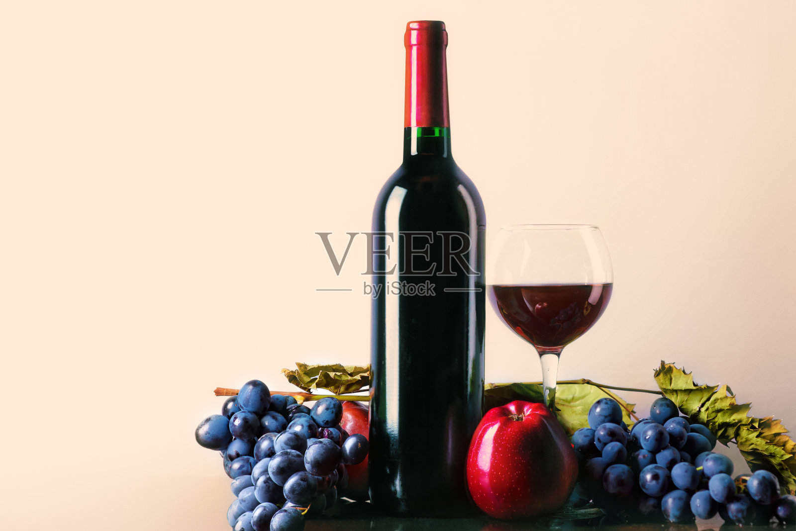 一杯和一瓶红酒配上葡萄和苹果。灯光背景下的红酒照片摄影图片