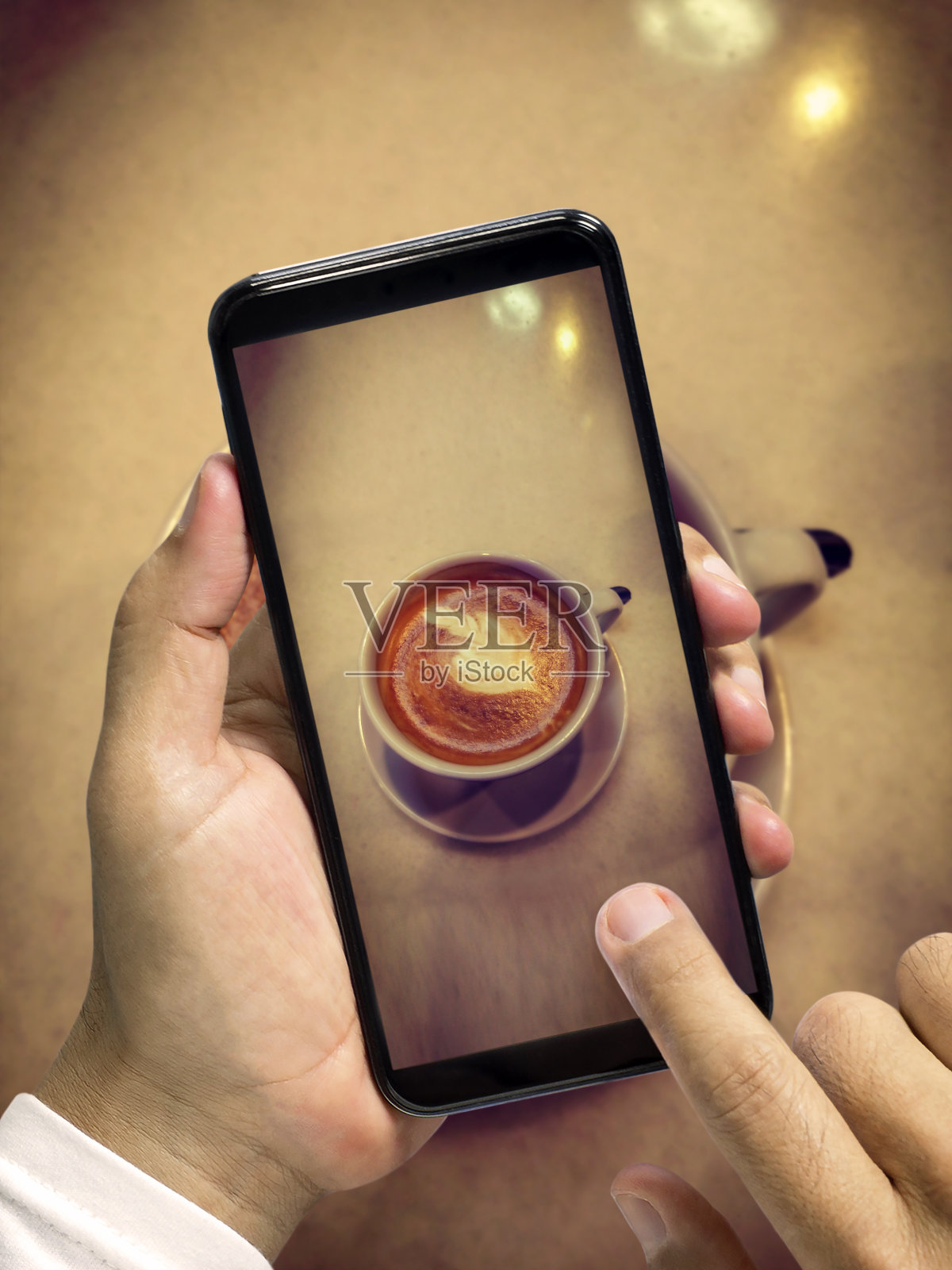 用智能手机给咖啡杯拍照。男人的手拿着智能手机拍摄一杯美丽的咖啡。照片摄影图片