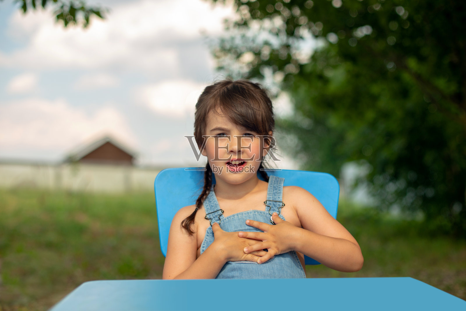 一个奇怪的女孩坐在夏日花园的一张桌子旁照片摄影图片