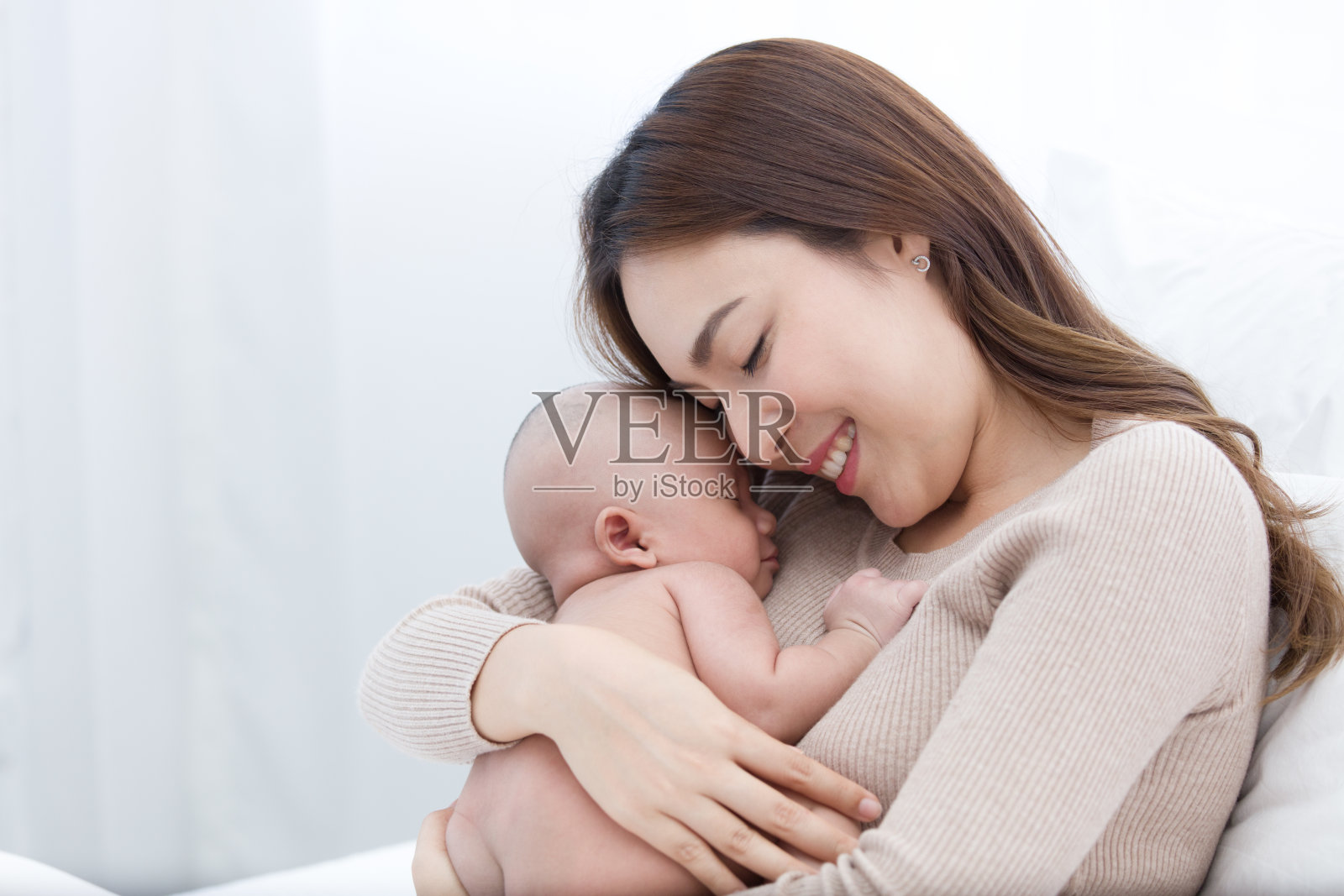 美丽的妈妈抱着刚出生的婴儿，婴儿在胸前睡觉。亚洲母亲用额头互相触碰，表示爱和保护。照片摄影图片