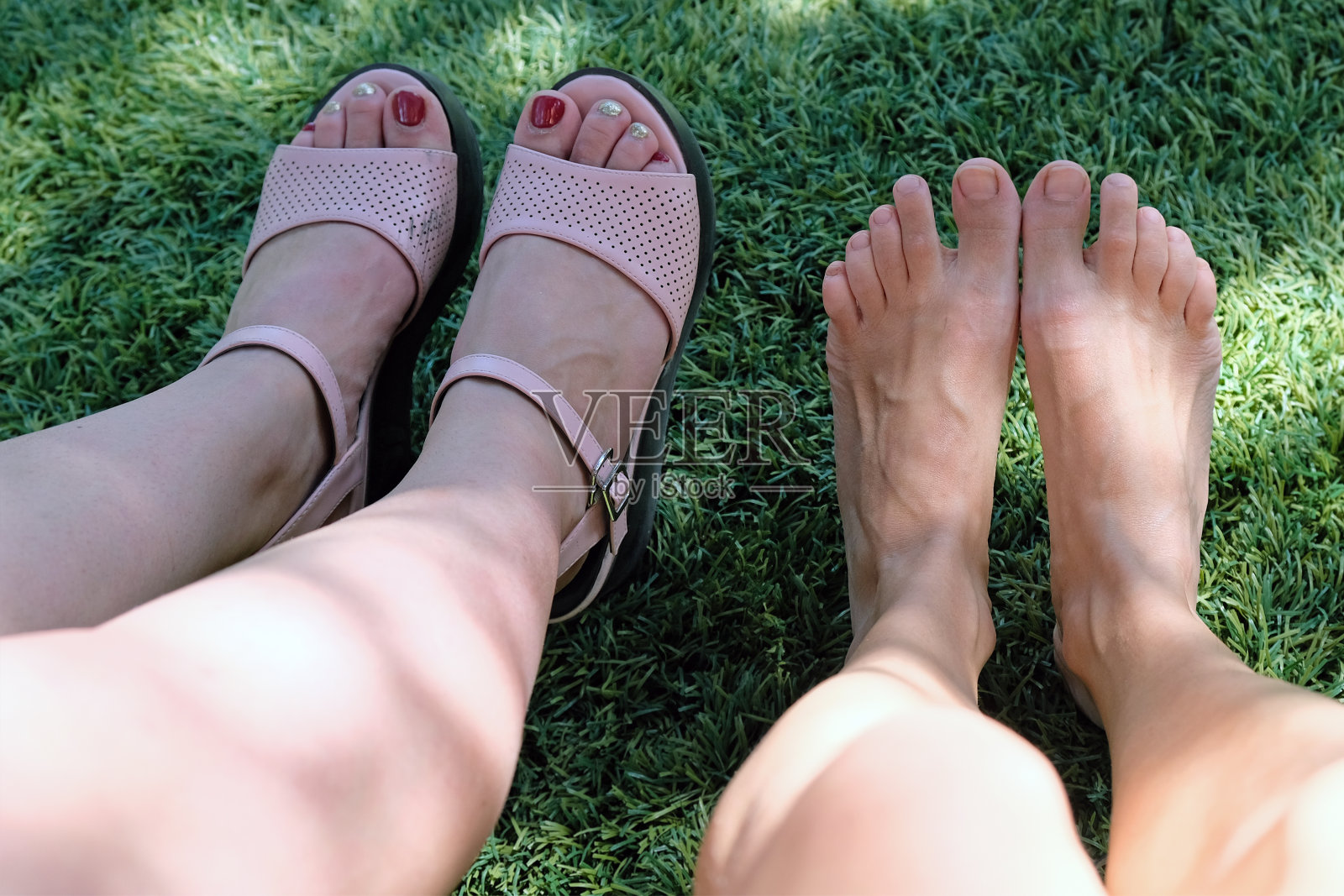 两个女孩的腿和脚，一个女孩没穿鞋，另一个穿着粉色凉鞋照片摄影图片