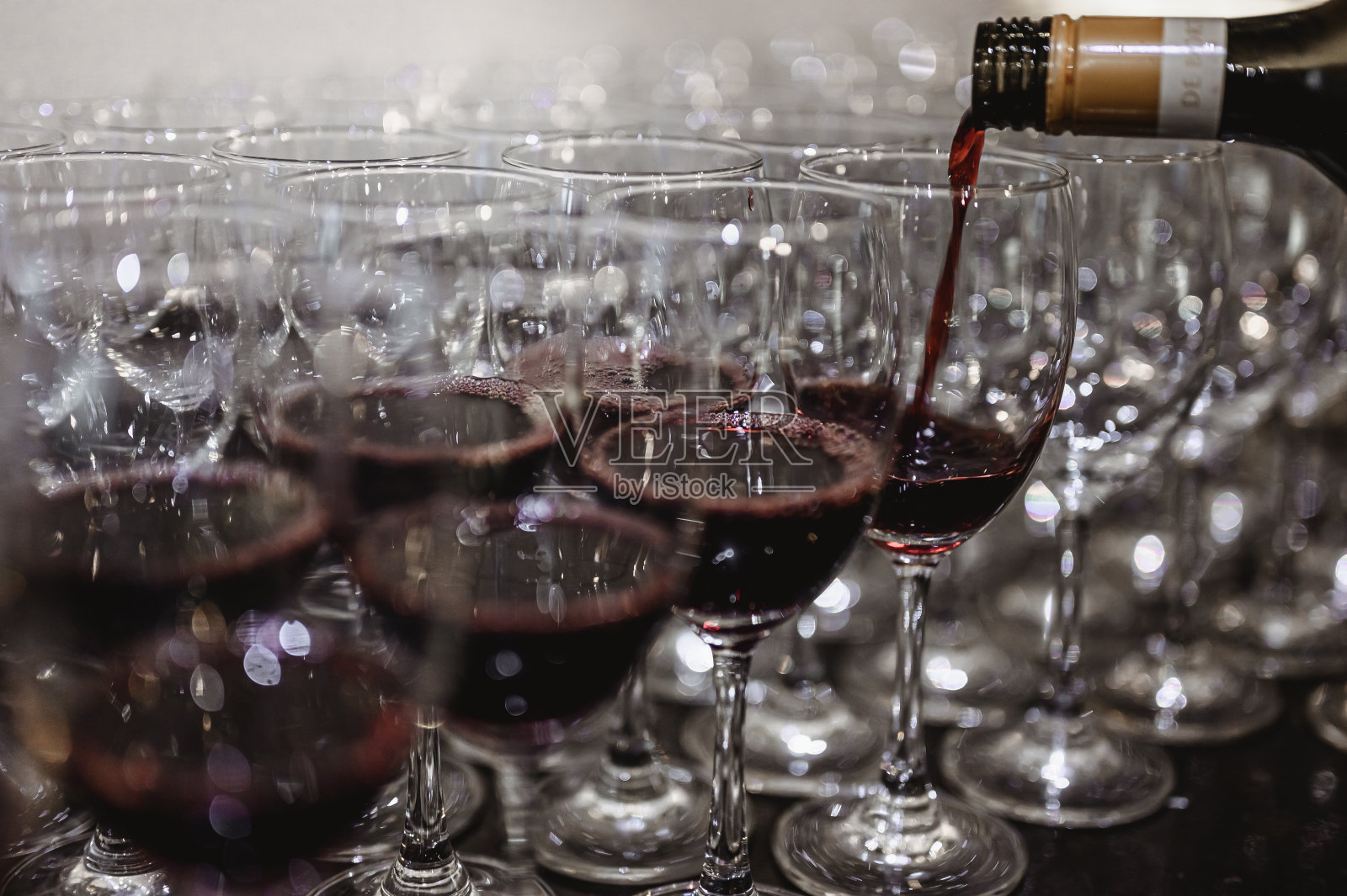 酒保正在把红酒倒进玻璃杯里，吧台上有许多空玻璃杯。模糊的背景。葡萄酒，品酒，斟酒，酒保，饮料，晚餐概念。照片摄影图片