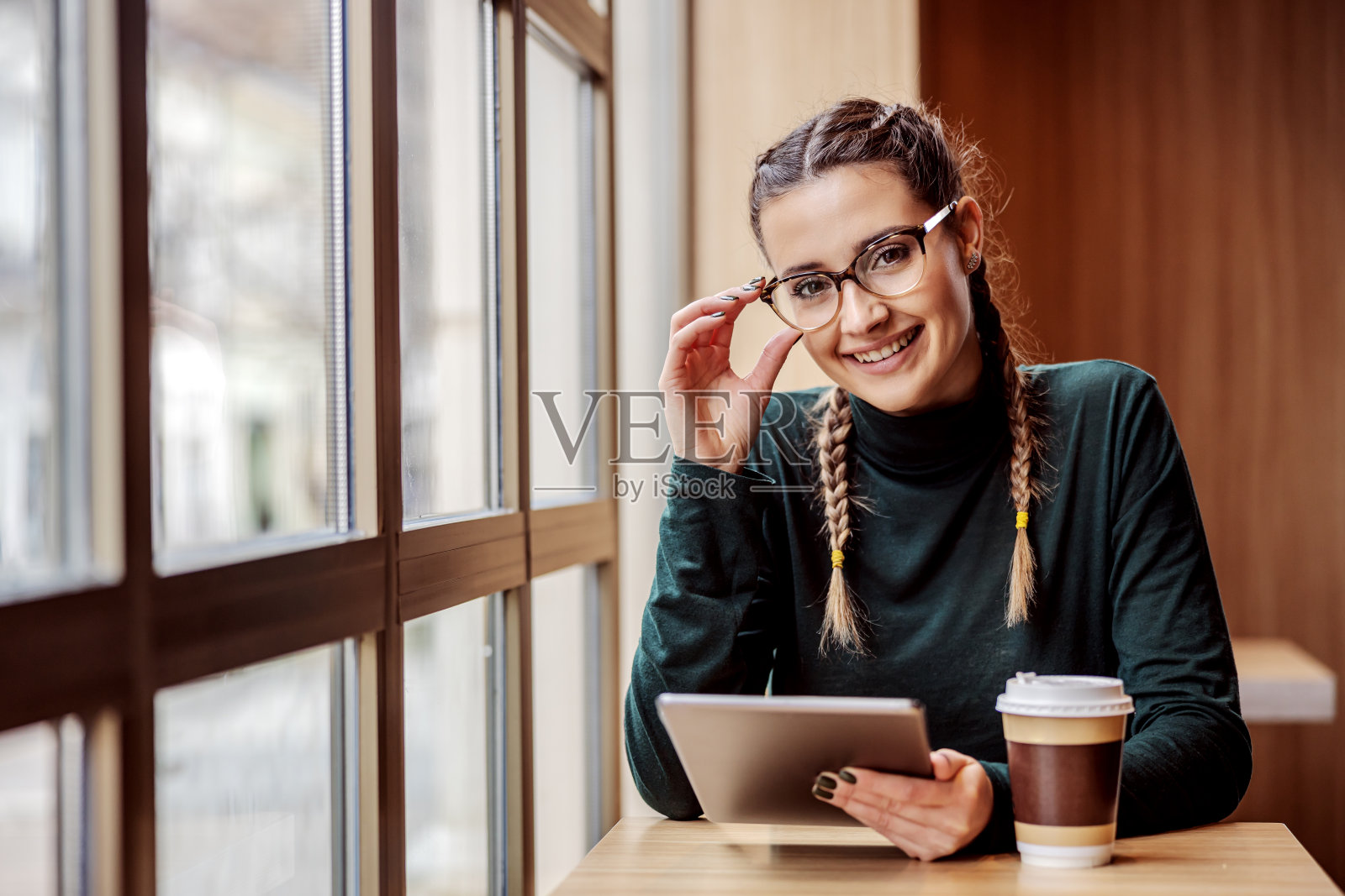 微笑的女大学生坐在咖啡店里，拿着平板电脑，看着相机。全球通信的概念。照片摄影图片