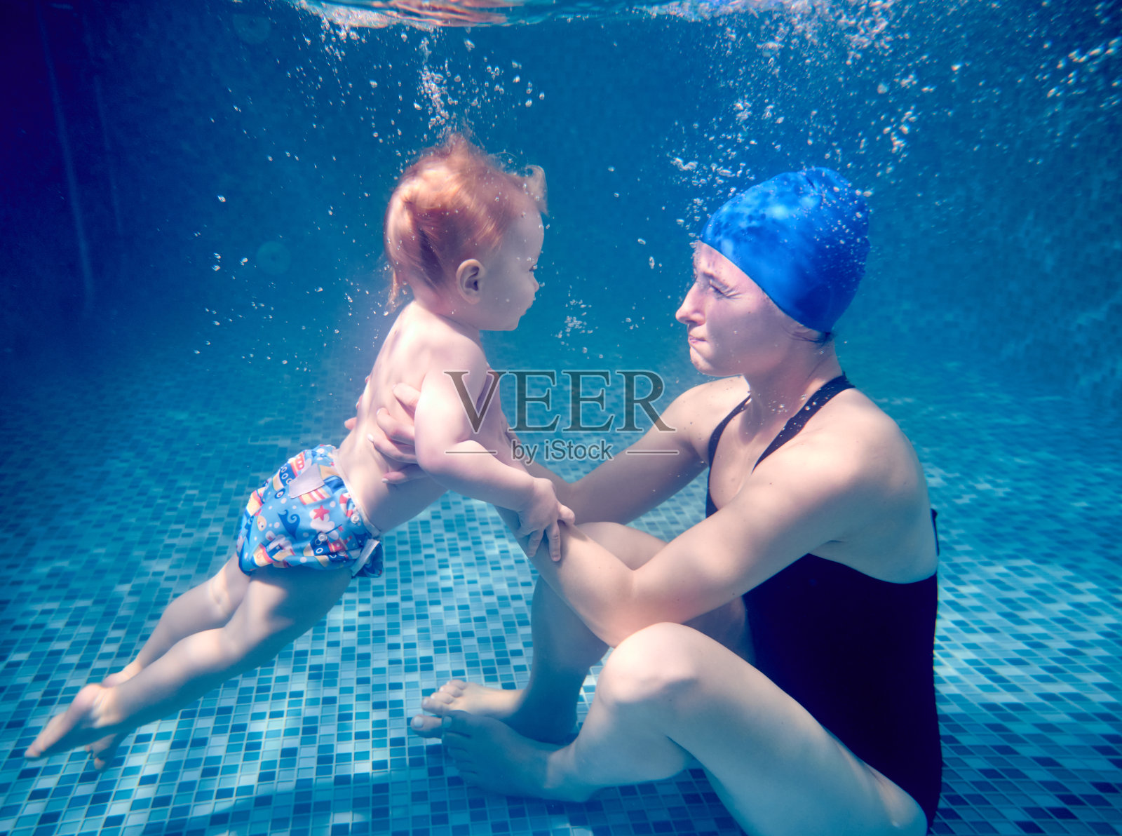 年轻的母亲和可爱的儿子在水下游泳。照片摄影图片